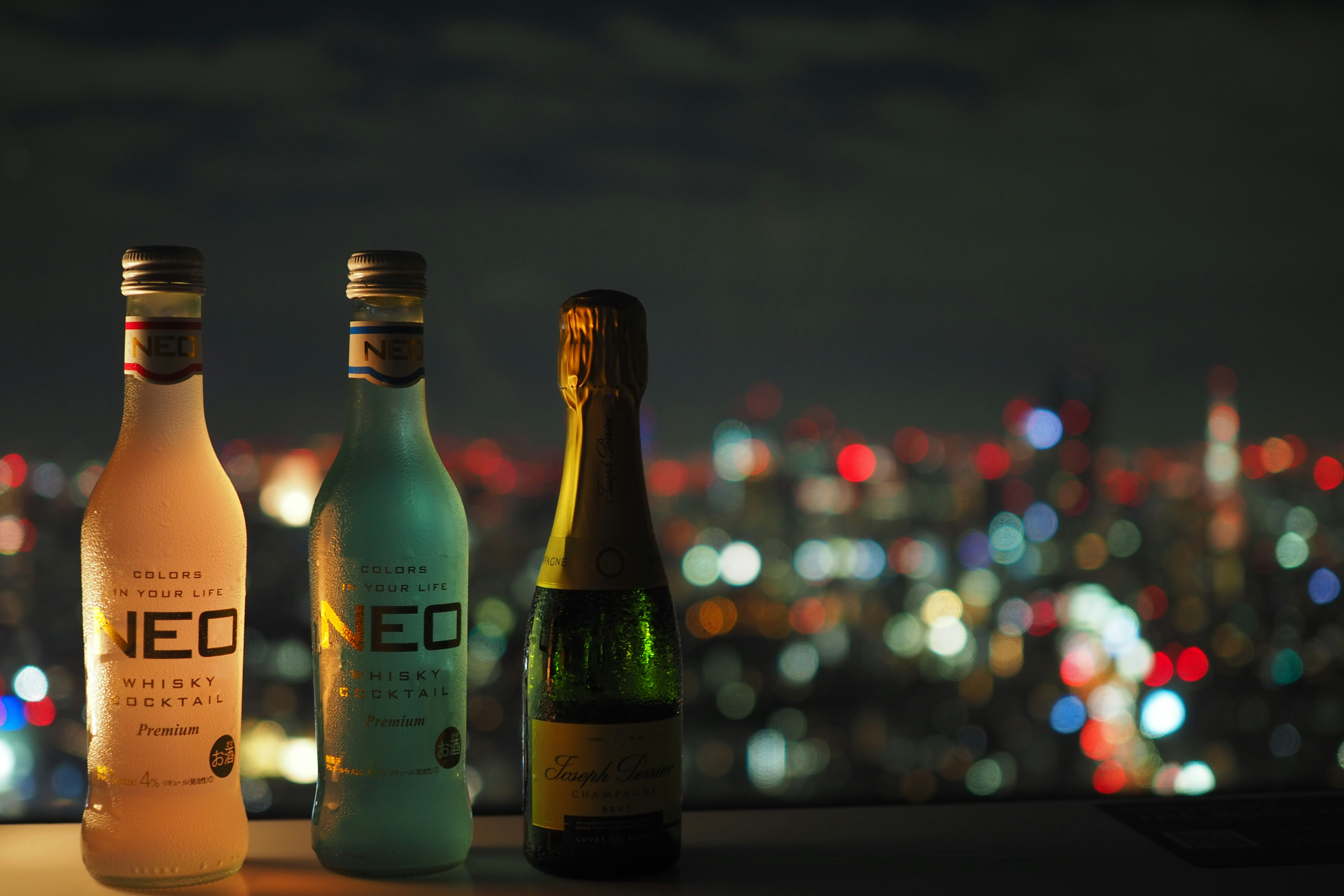 Botellas de bebida NEO y champán frente a un horizonte nocturno