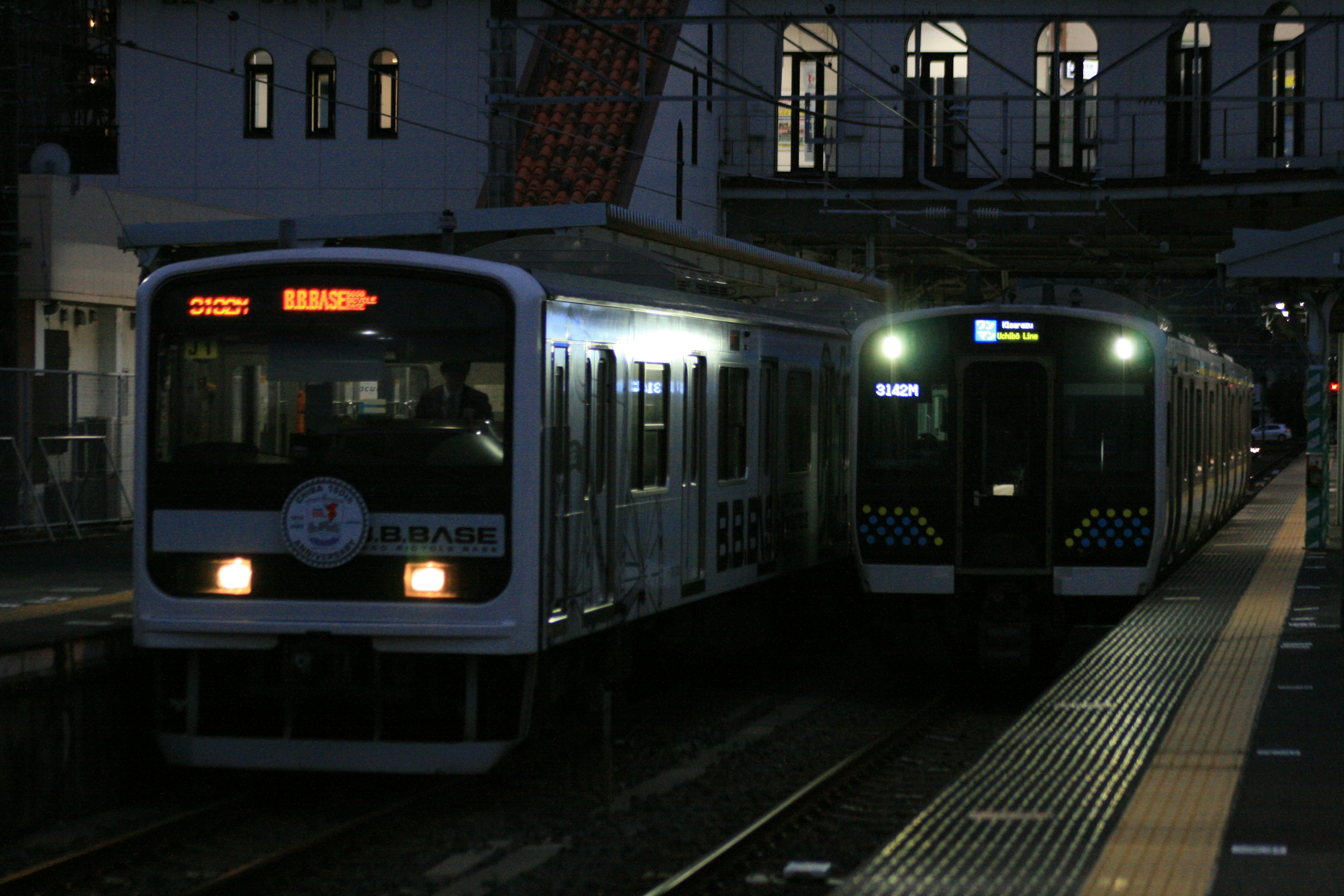 Dos trenes detenidos en una estación durante la noche con un edificio al fondo