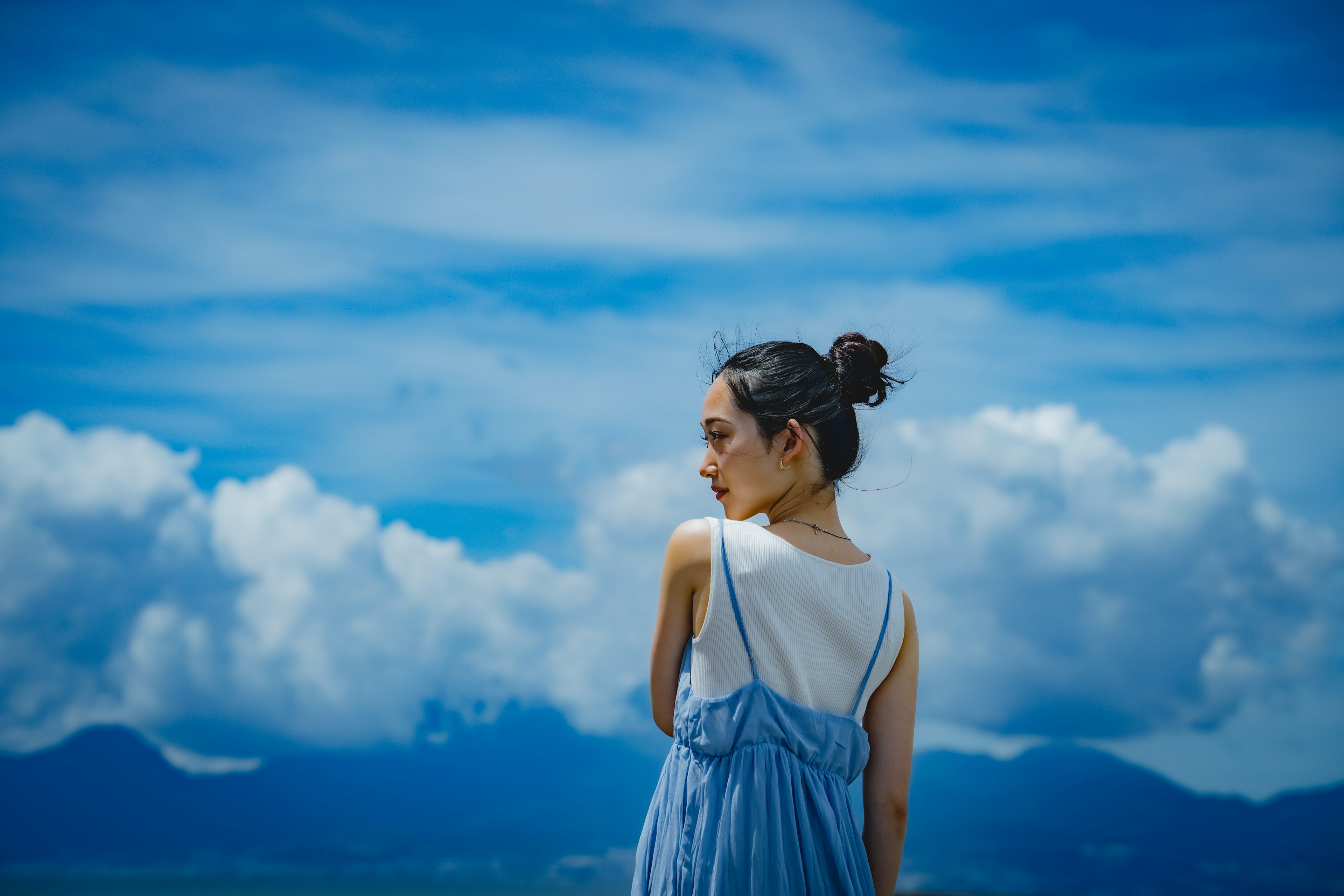 Una mujer vista de espaldas contra un fondo de cielo azul y nubes