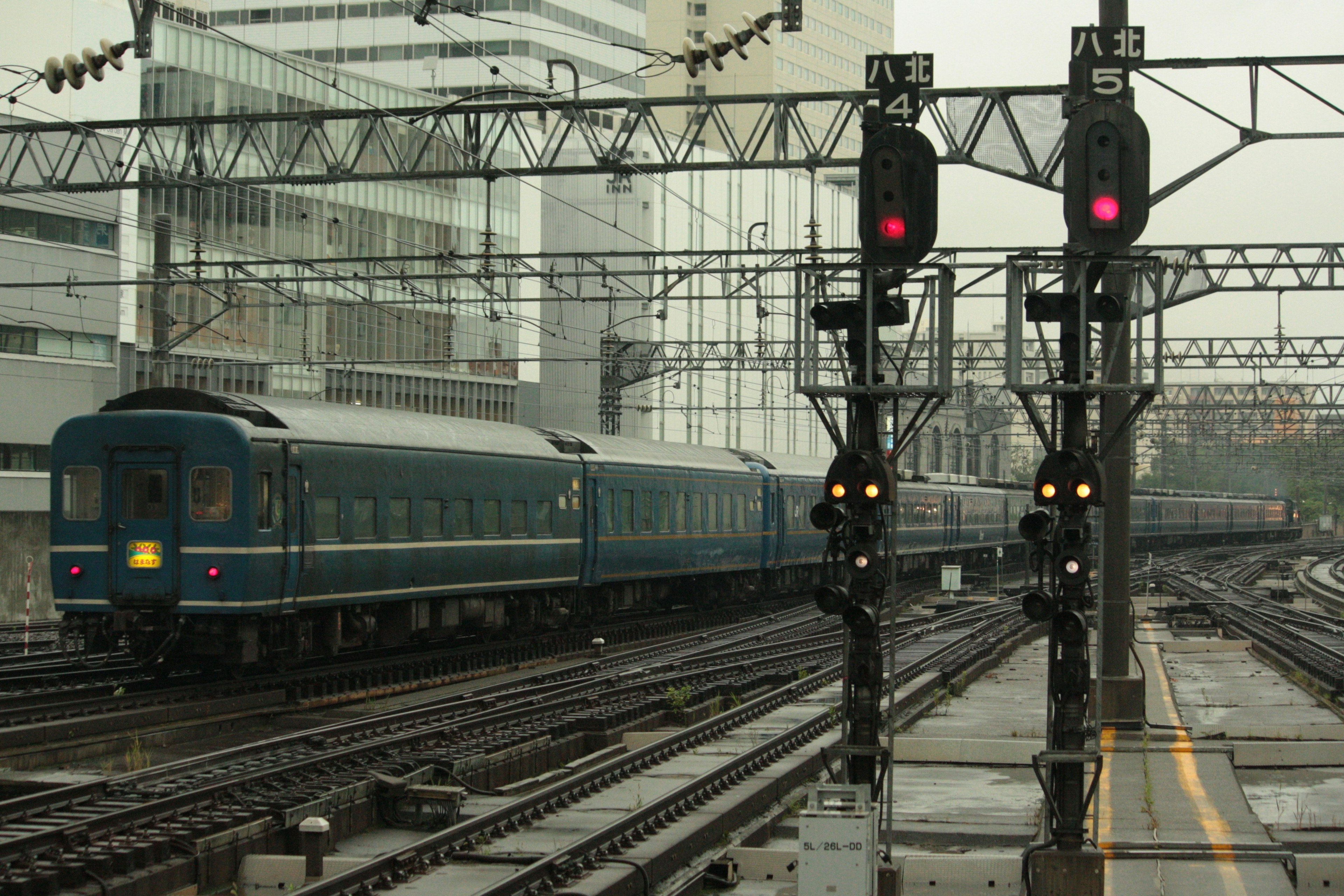 Ein blauer Zug, der an Signalen an einem regnerischen Tag am Bahnhof vorbeifährt