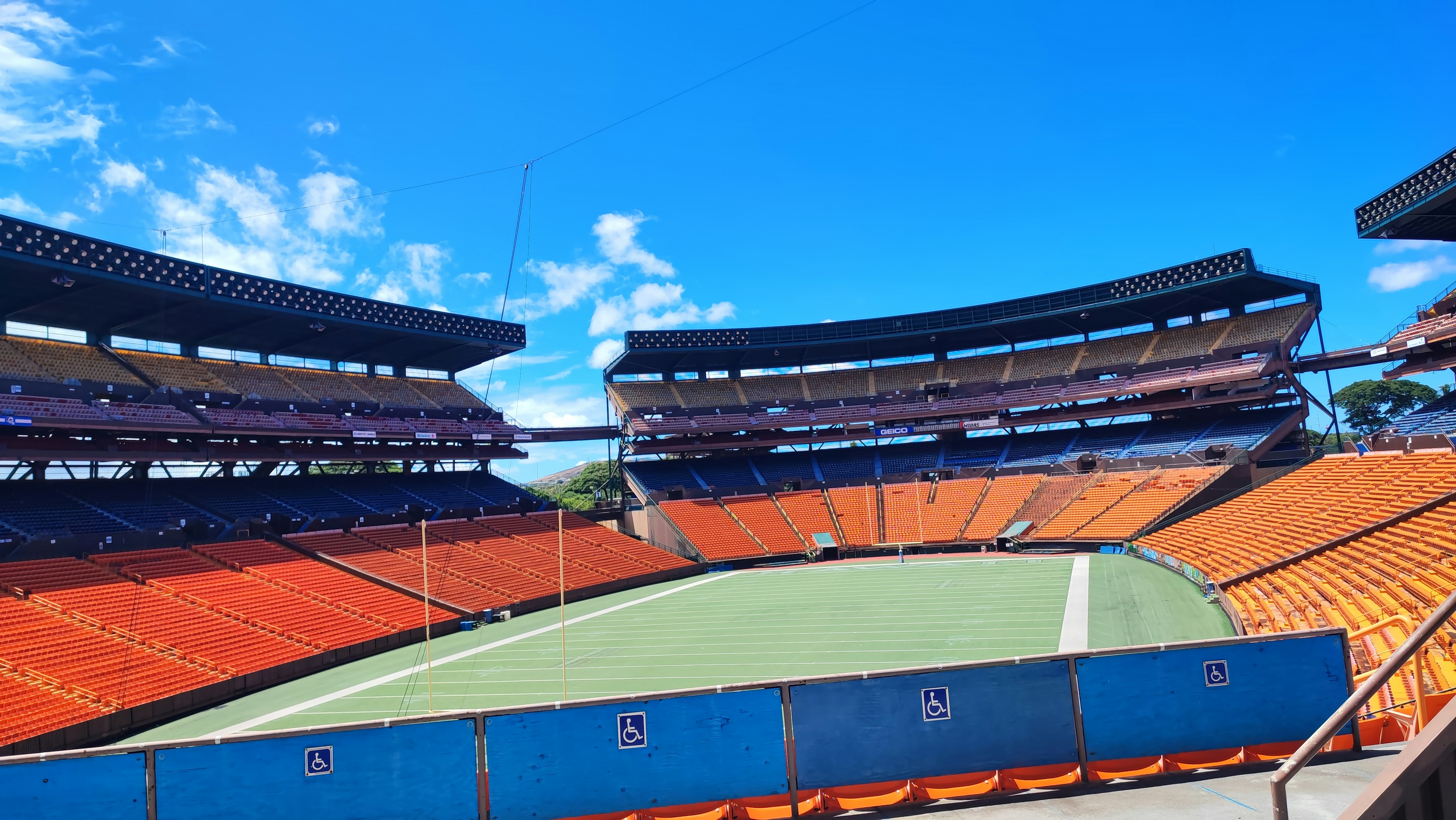 Stadioninnenraum unter blauem Himmel mit orangefarbenen Sitzen und grünem Feld