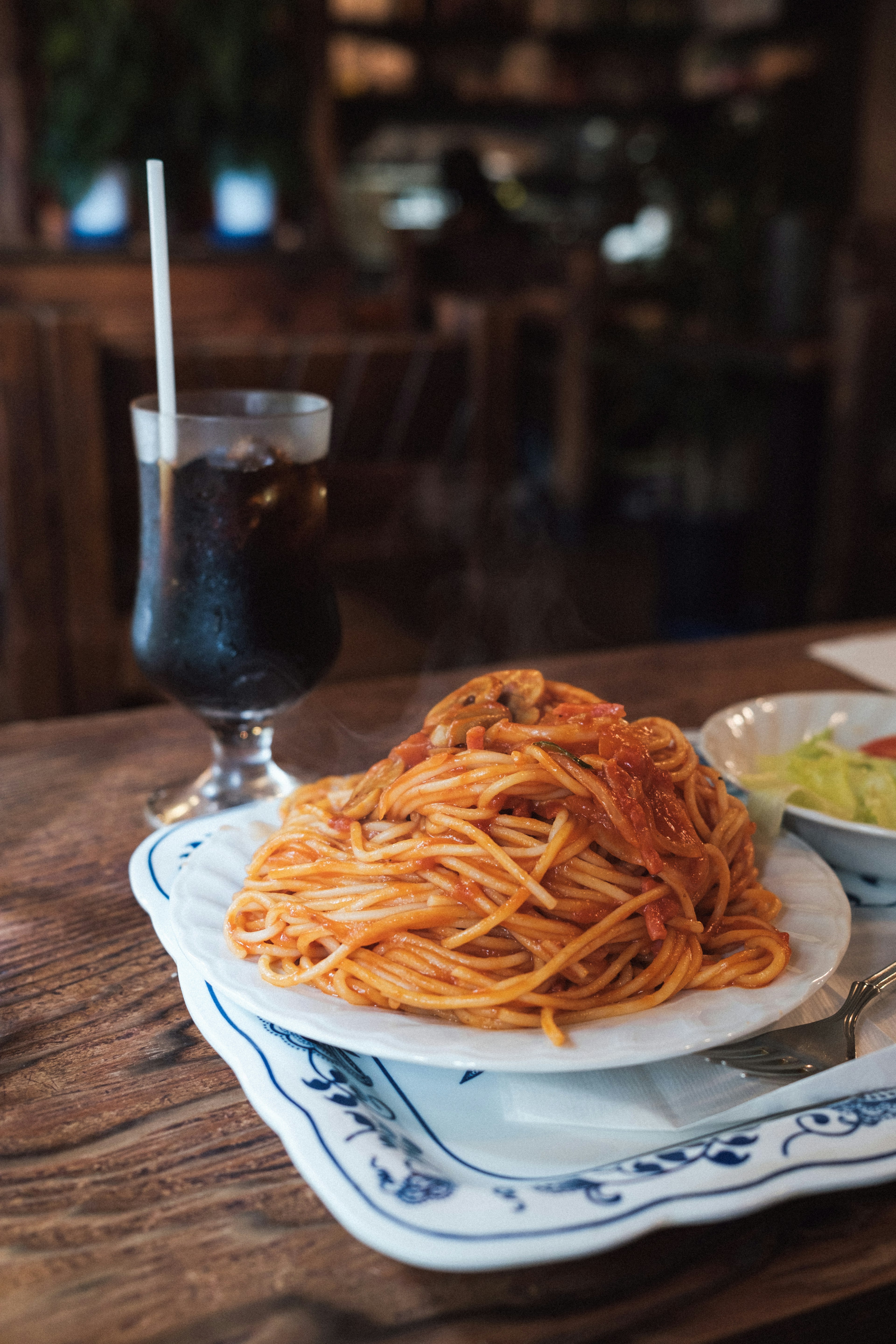 Plato de espagueti con un vaso de cola sobre una mesa de madera