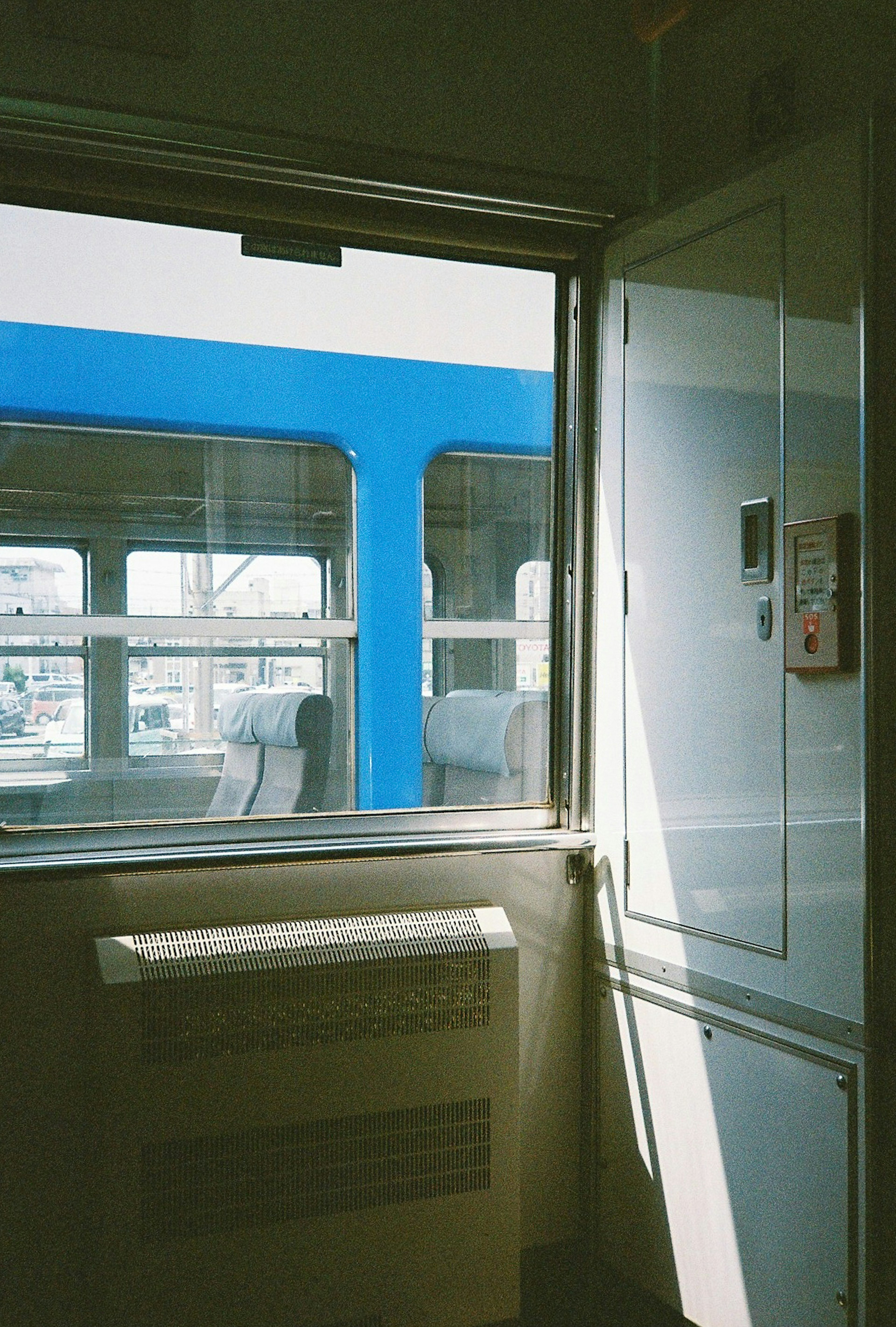 Interior view of a train with a blue train visible through the window and sunlight streaming in