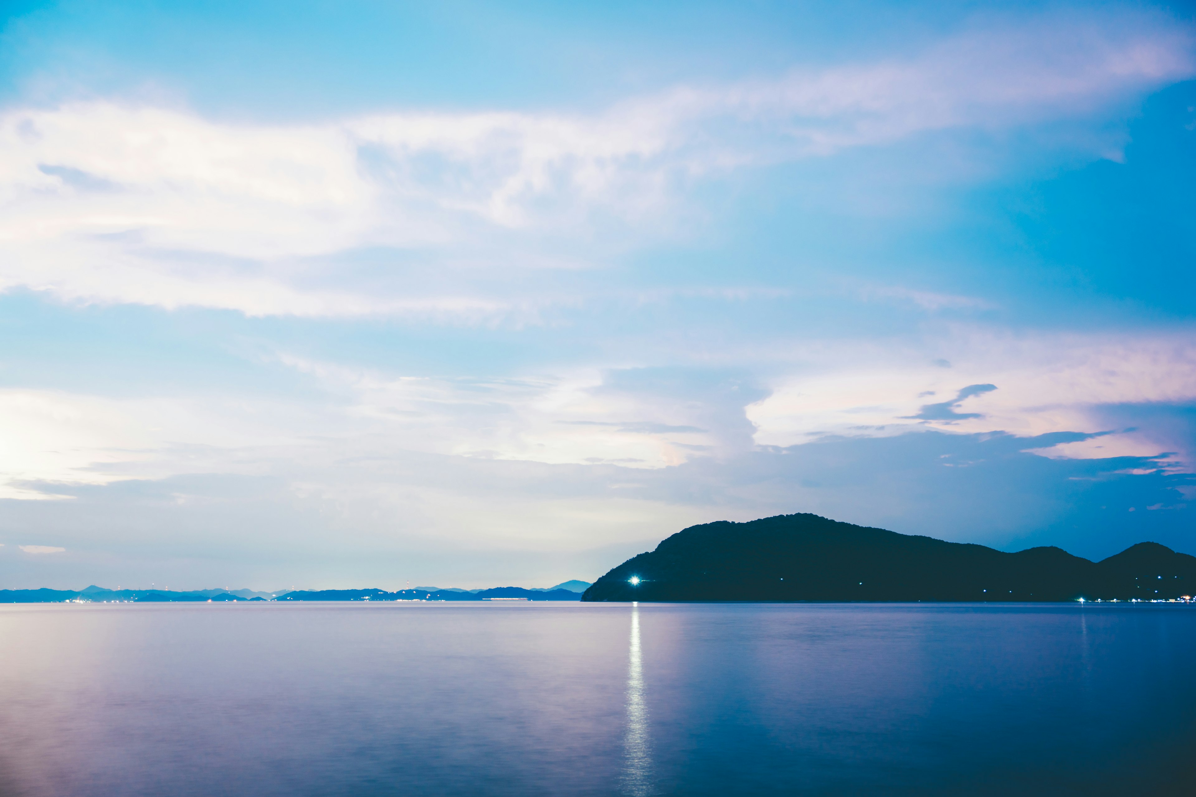 Pemandangan tenang laut biru dan langit dengan pegunungan di kejauhan