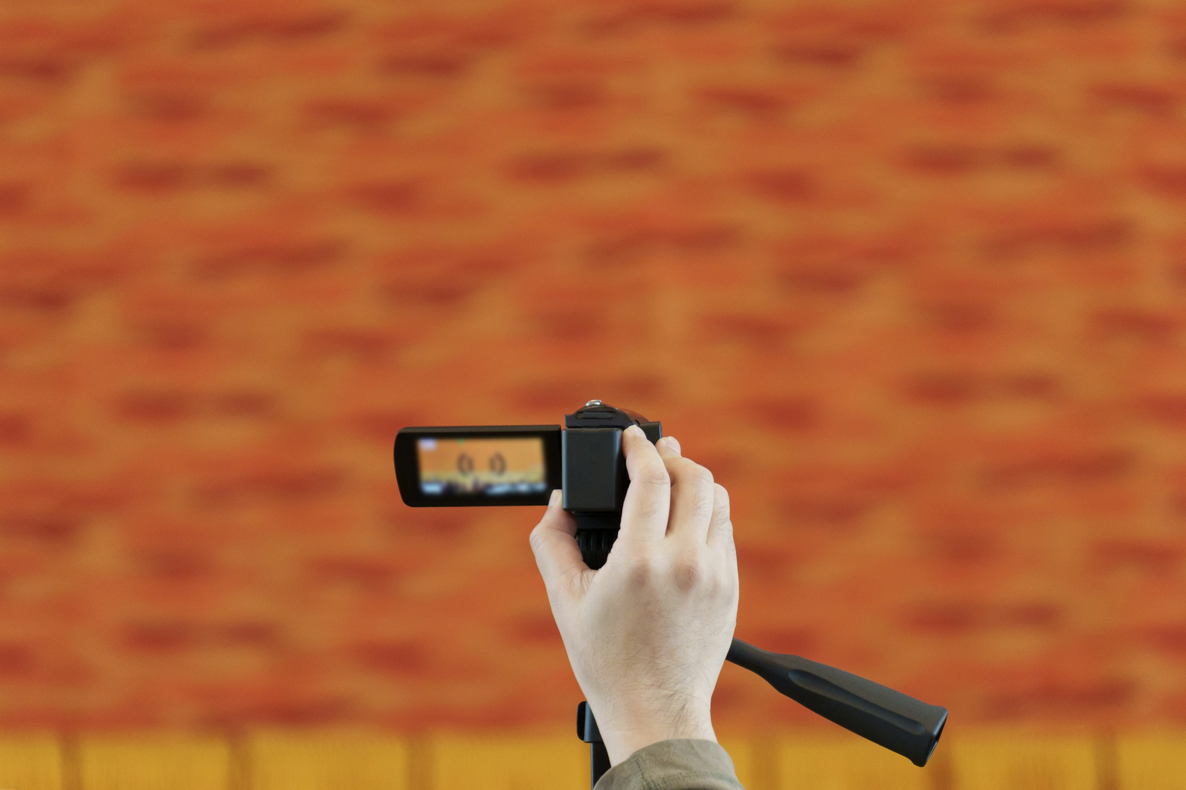 Hand holding a camera with an orange background