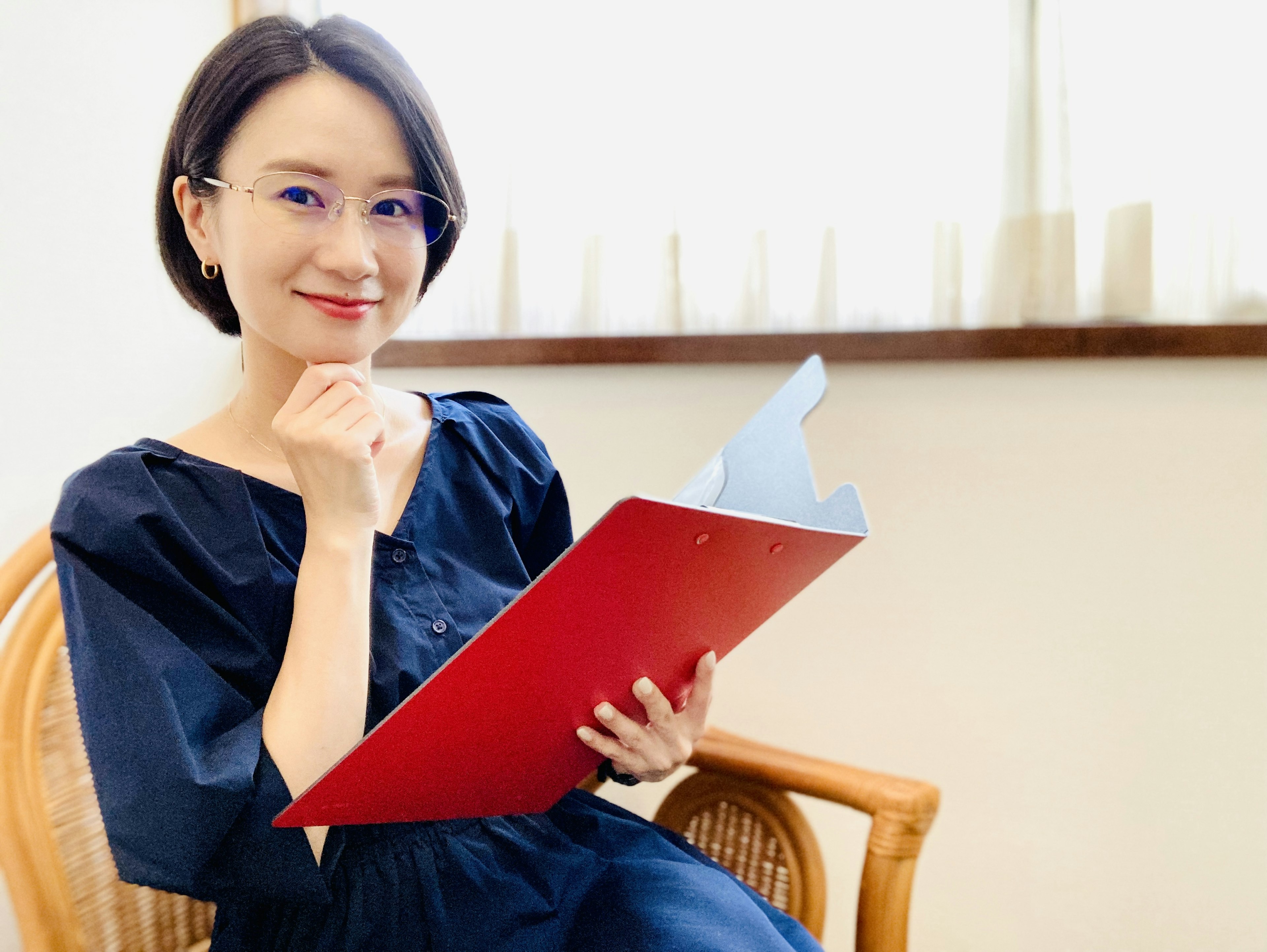 Woman in blue dress holding red folder smiling thoughtfully