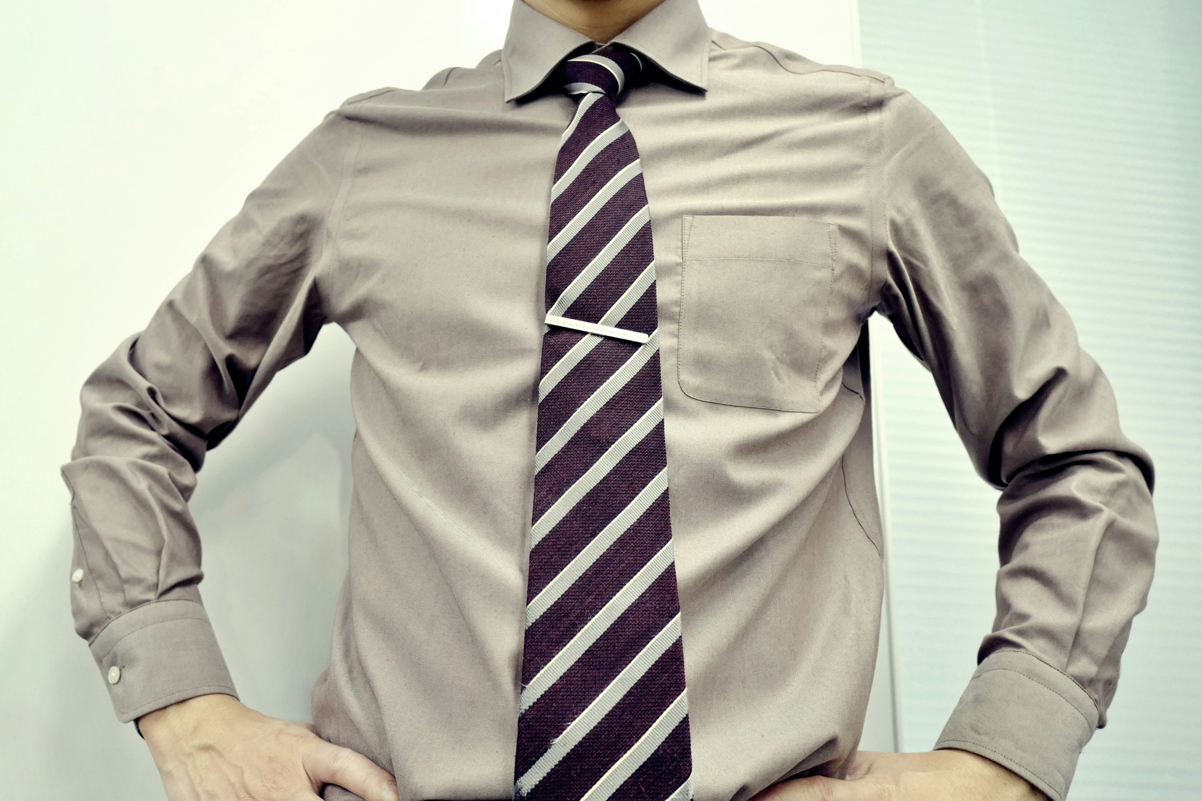 Un hombre posando con una camisa marrón claro y una corbata a rayas