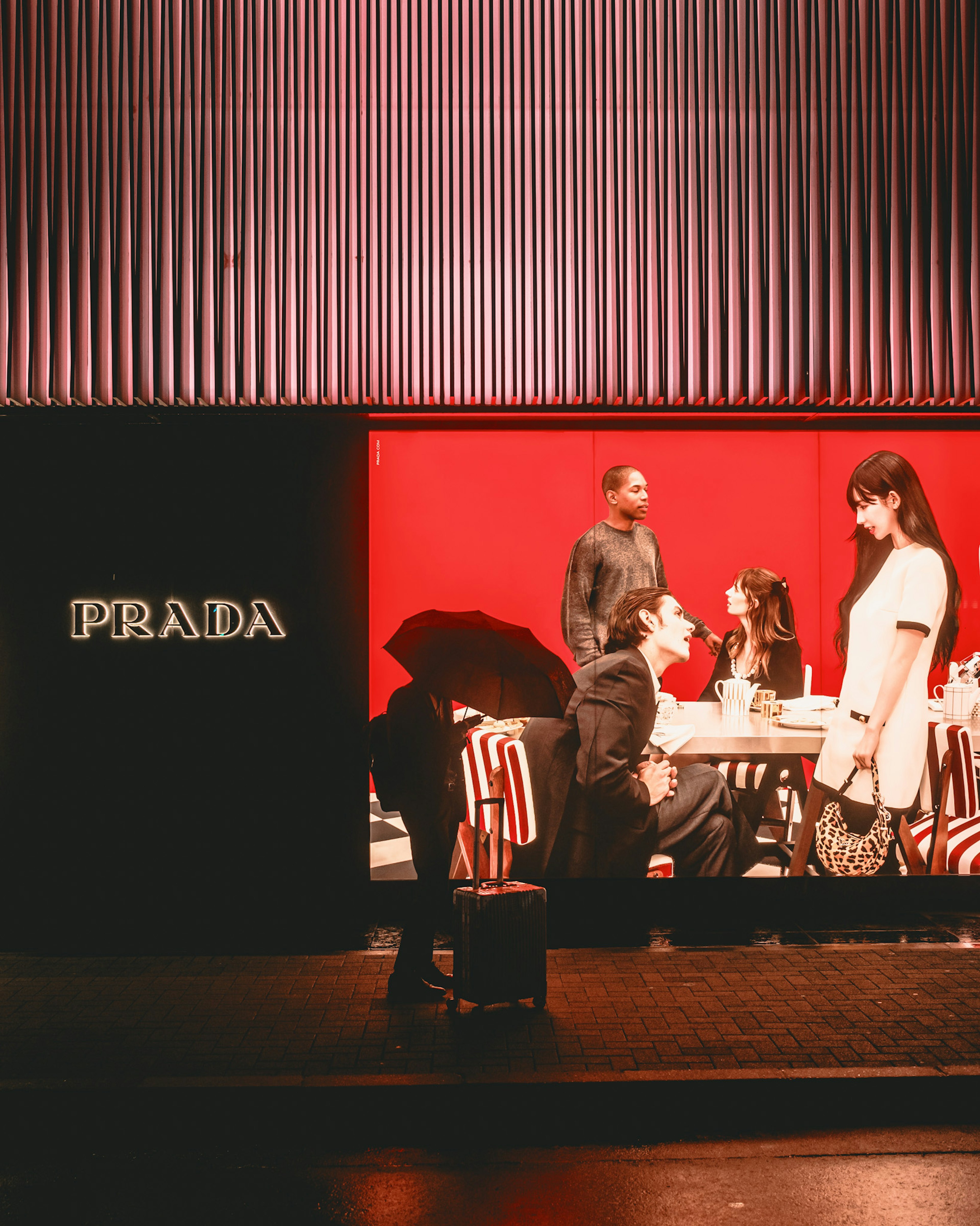 Scène de personnes dans une vitrine Prada avec un fond rouge présentant des personnages assis