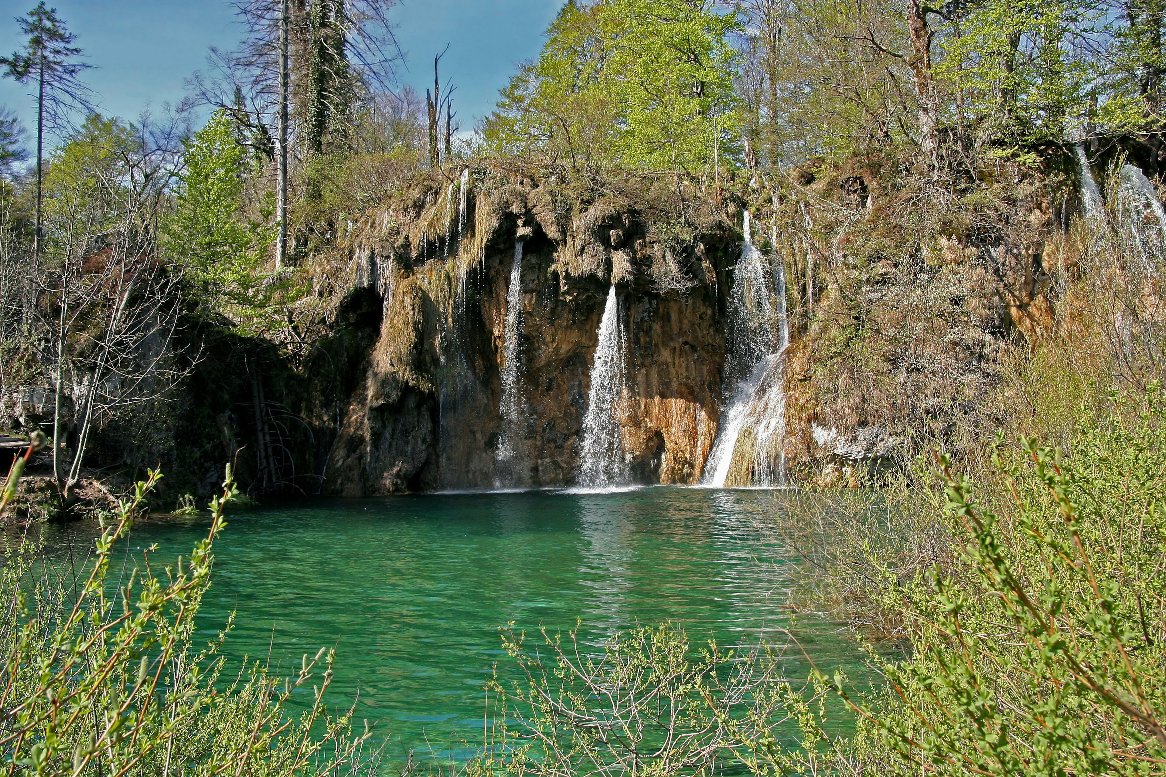 Scenic view of a turquoise lake with waterfalls surrounded by lush green trees