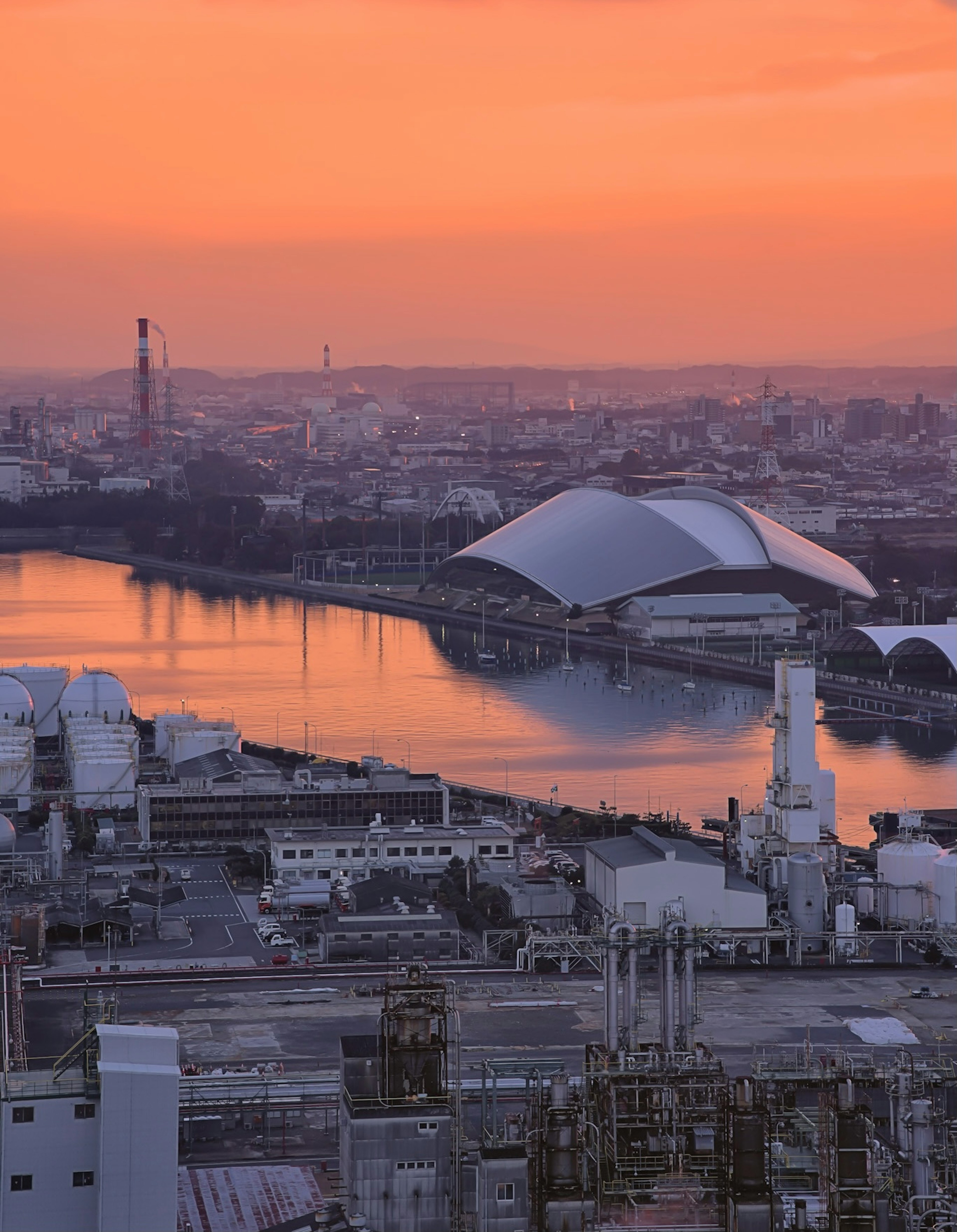 Industrial landscape at sunset featuring futuristic buildings by the river