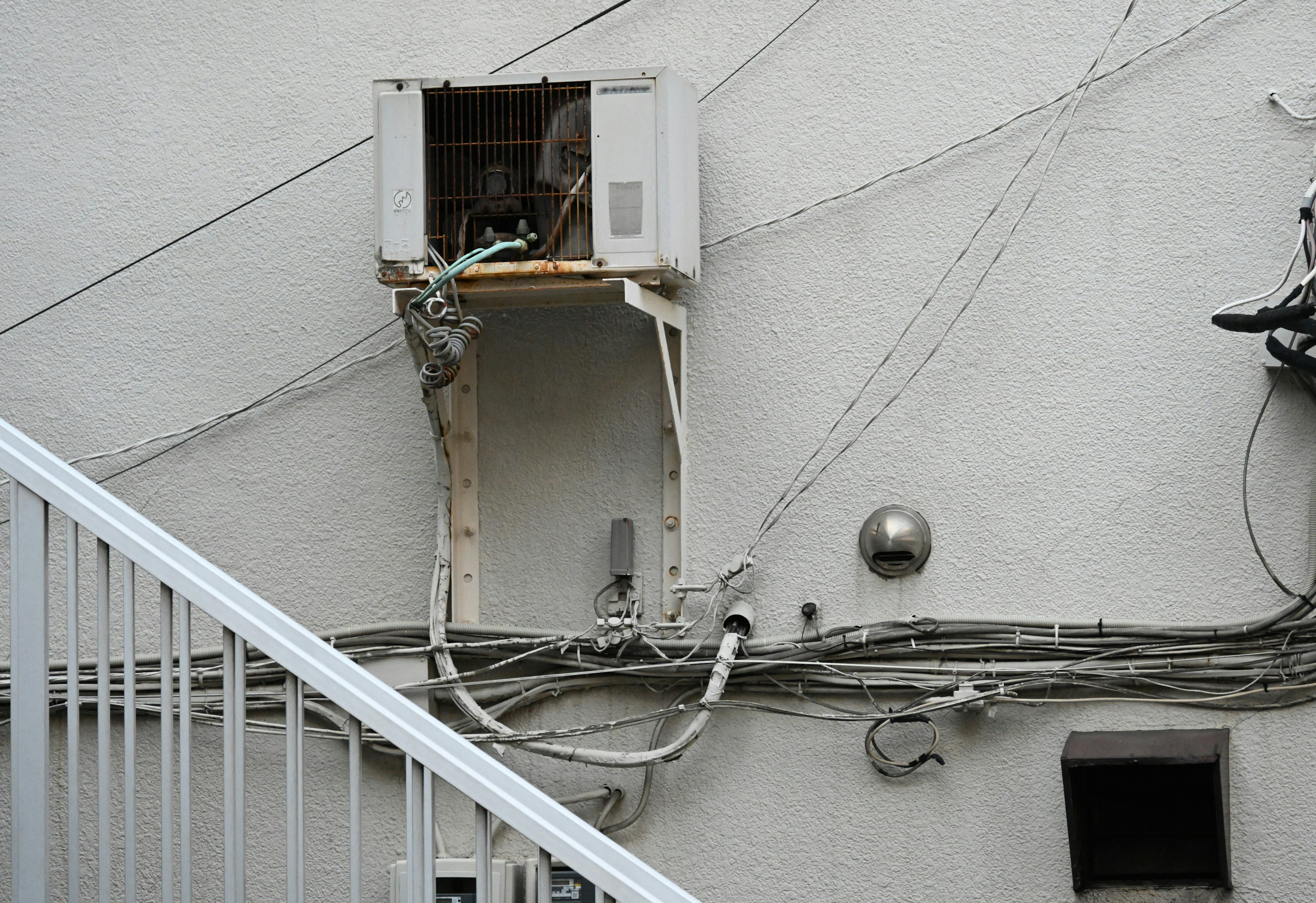 Old air conditioning unit mounted on a white wall with visible wiring