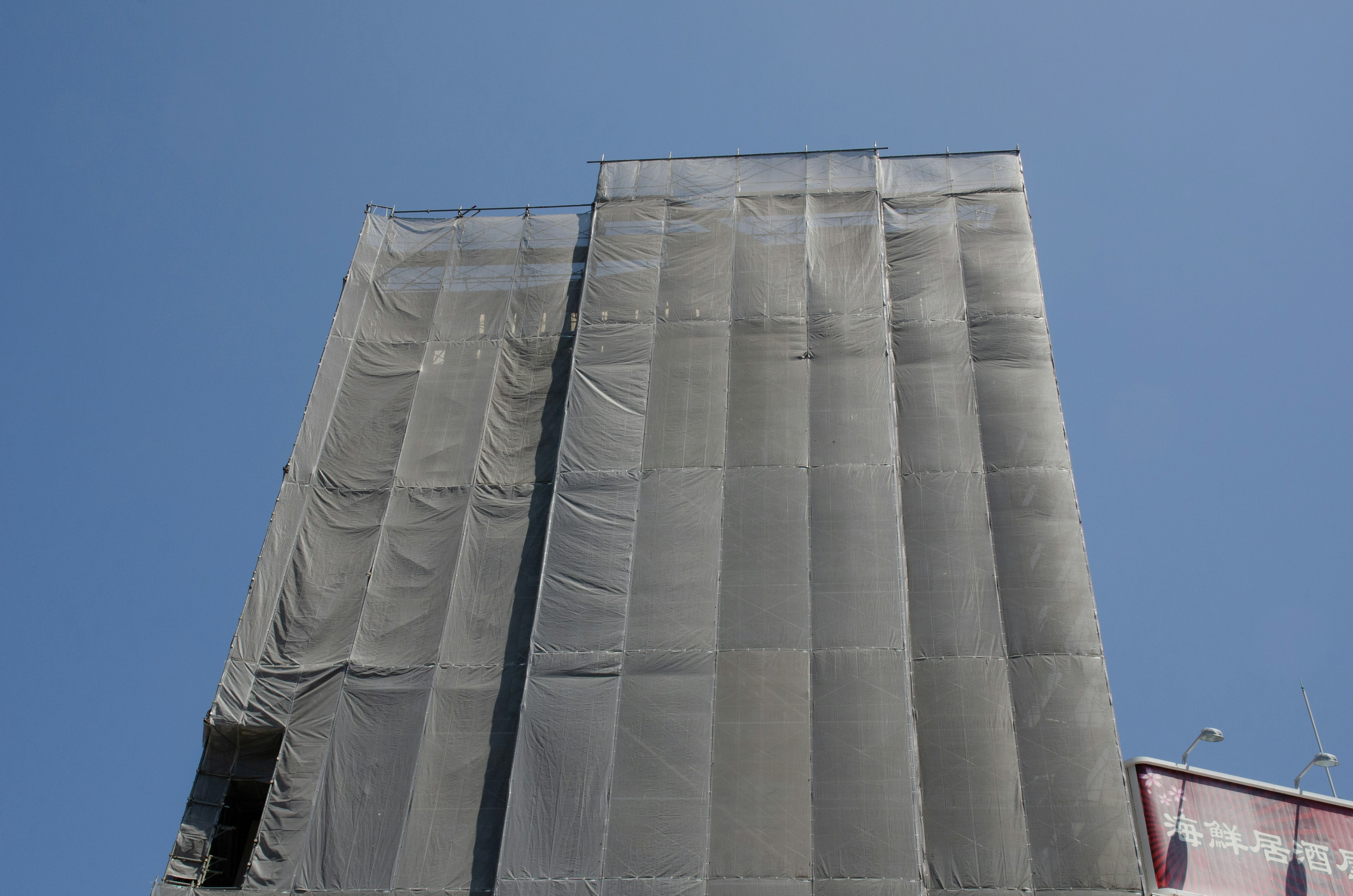 Building scaffolding covered with mesh against a clear blue sky