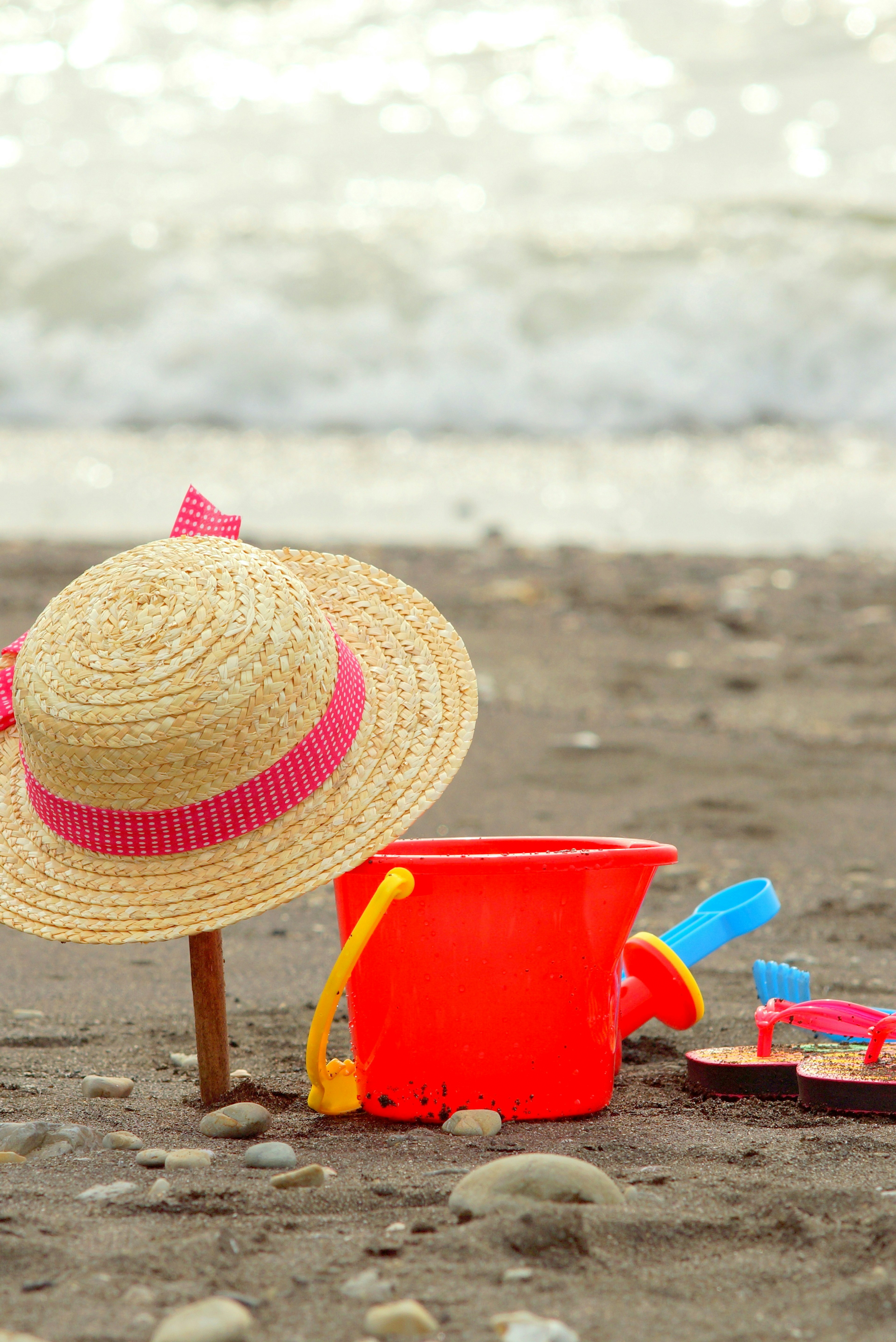 Seau rouge et chapeau en paille sur la plage