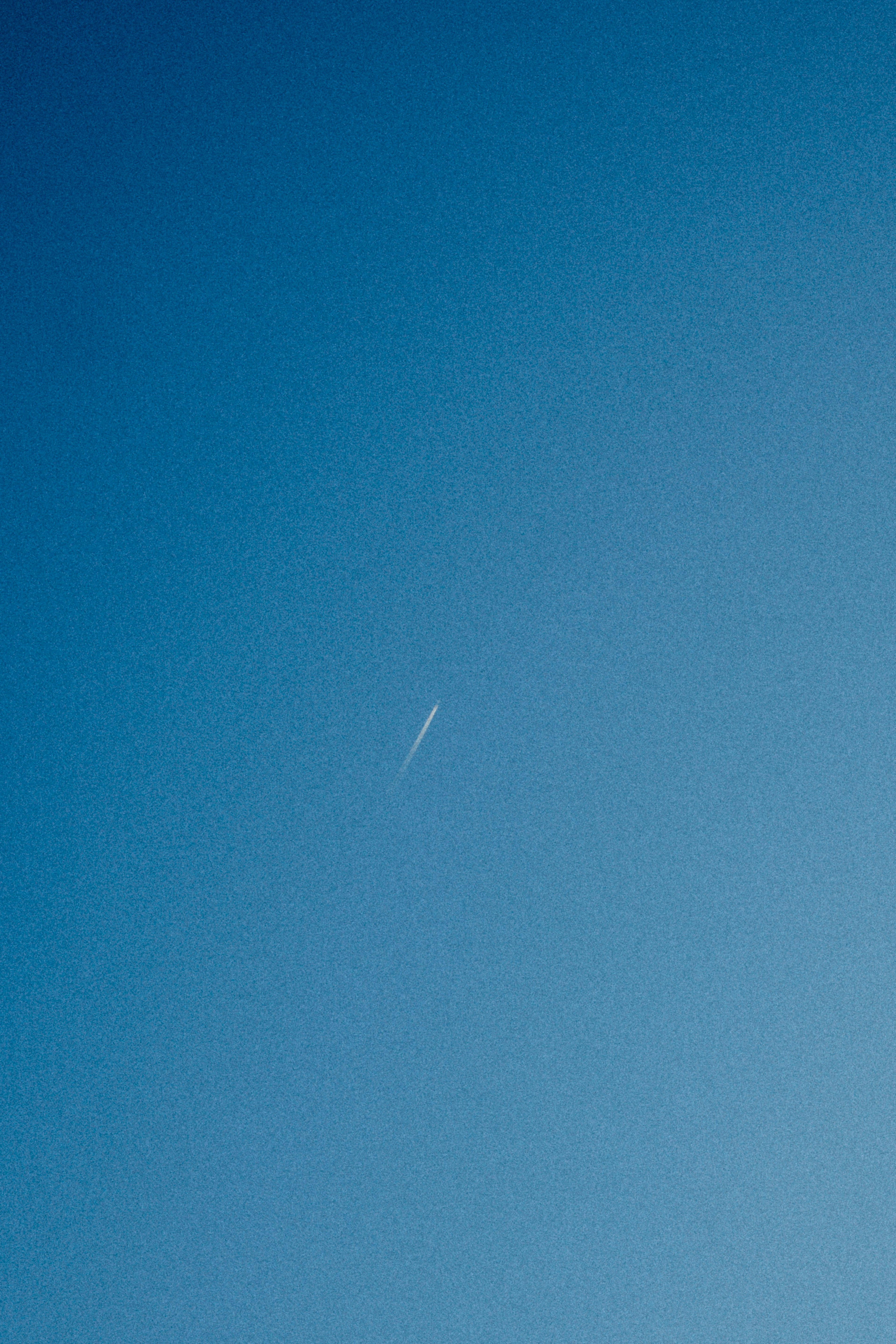 A simple view of a white contrail against a blue sky