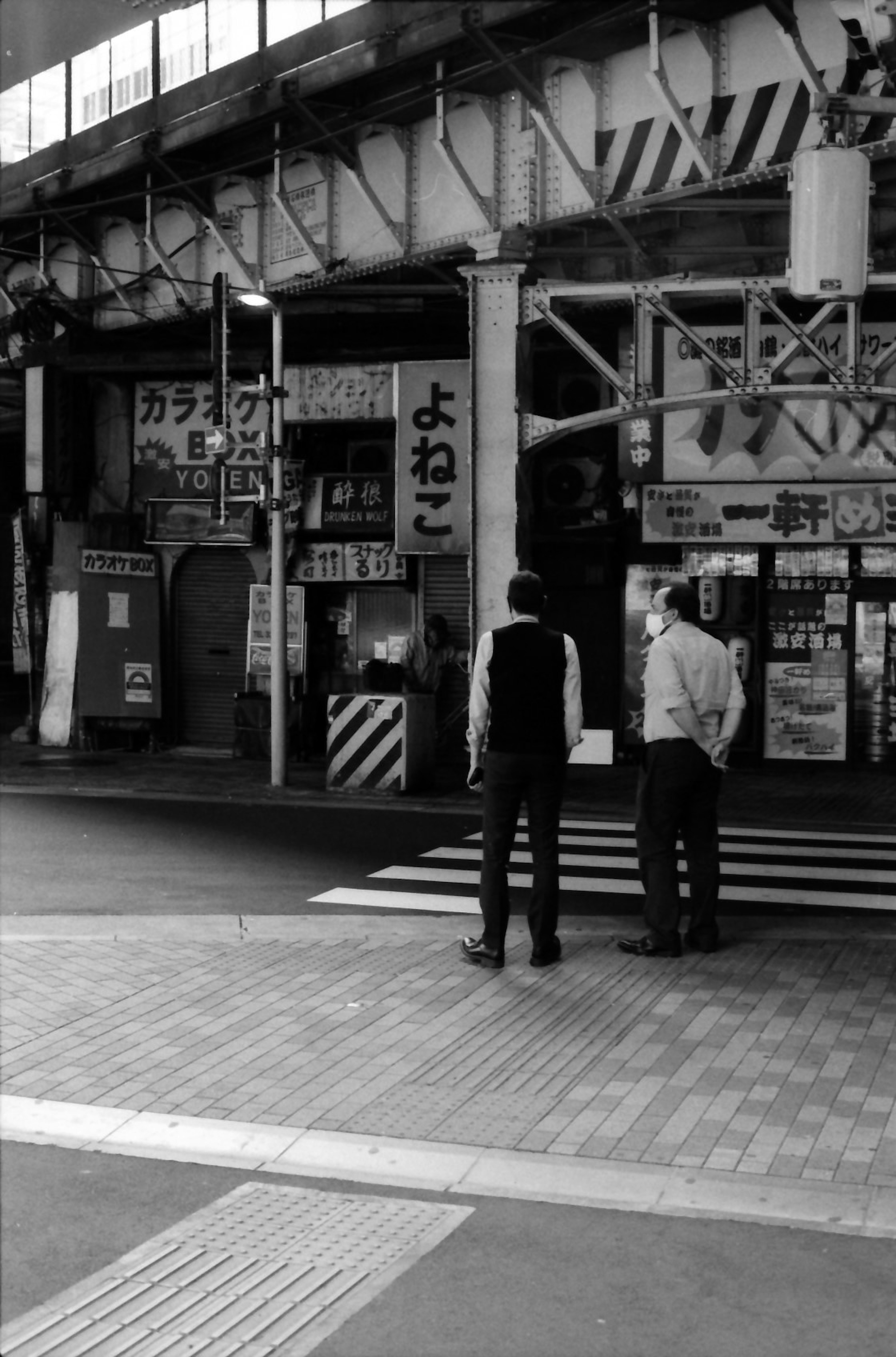 白黒の街角で二人の男性が立っている姿と古い看板が見える