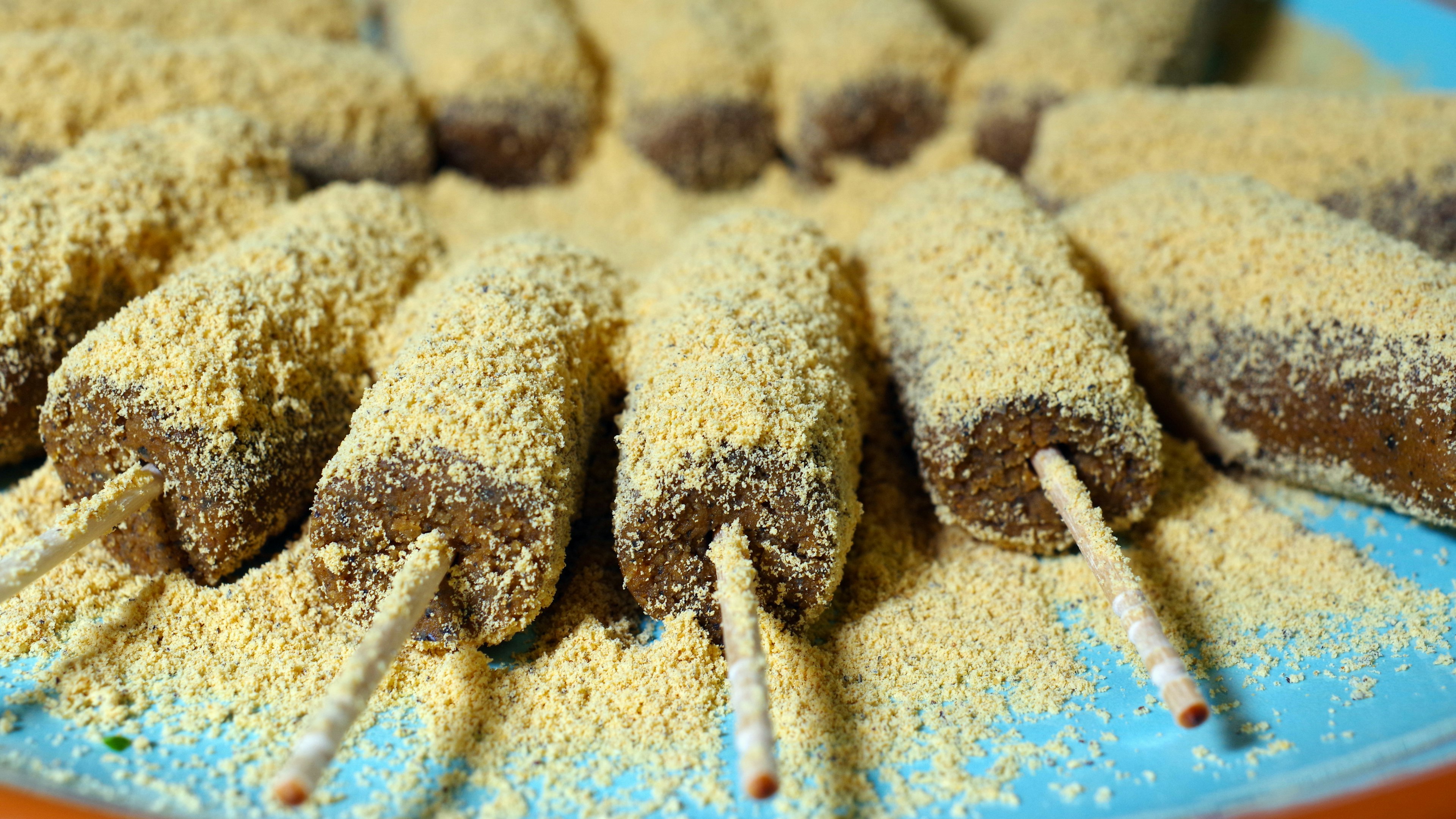 Friandises sucrées sur des bâtons recouvertes de poudre jaune disposées sur une assiette bleue