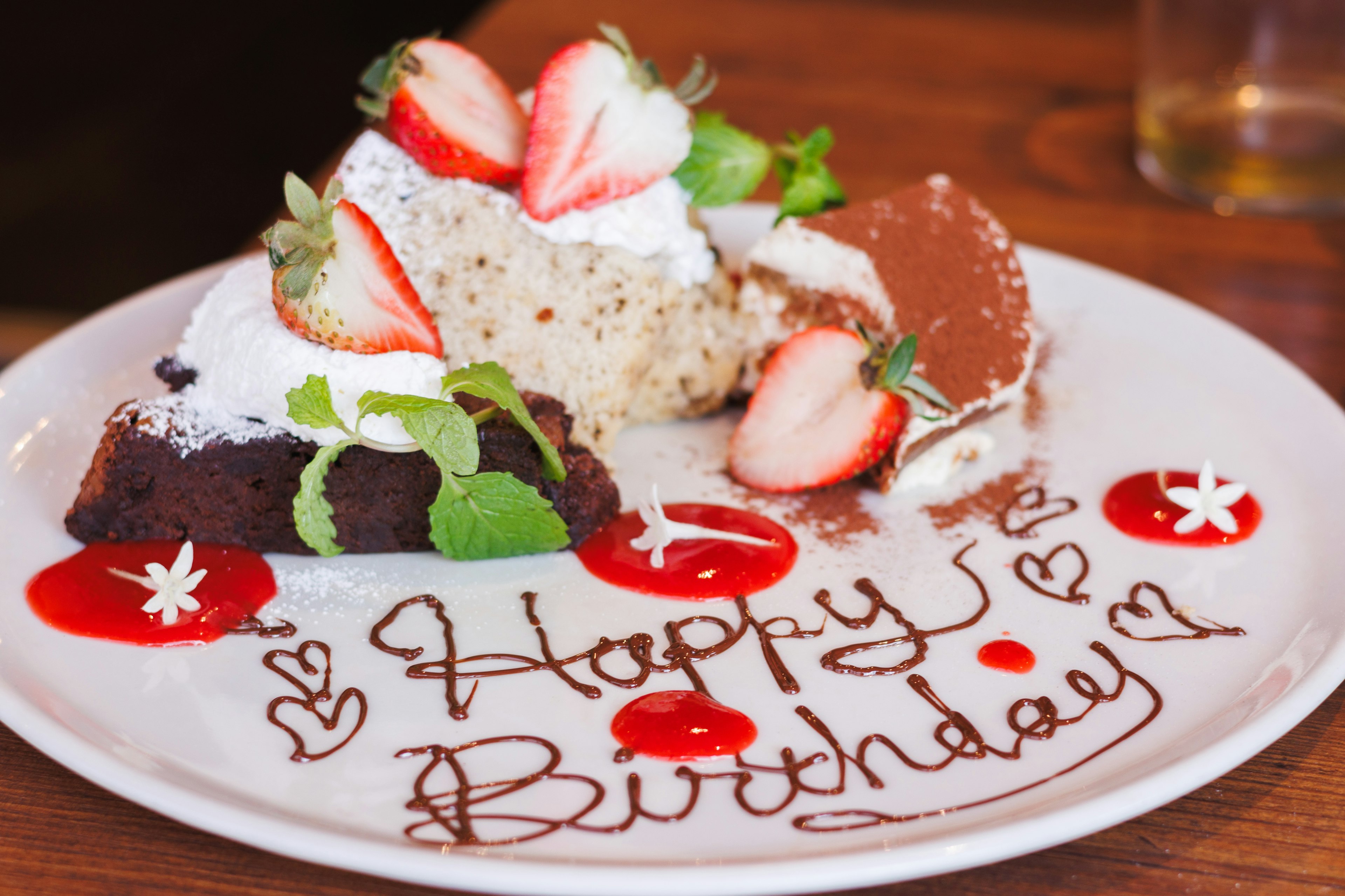 Pastel de cumpleaños con fresas y menta en un plato con Feliz Cumpleaños escrito en salsa de chocolate