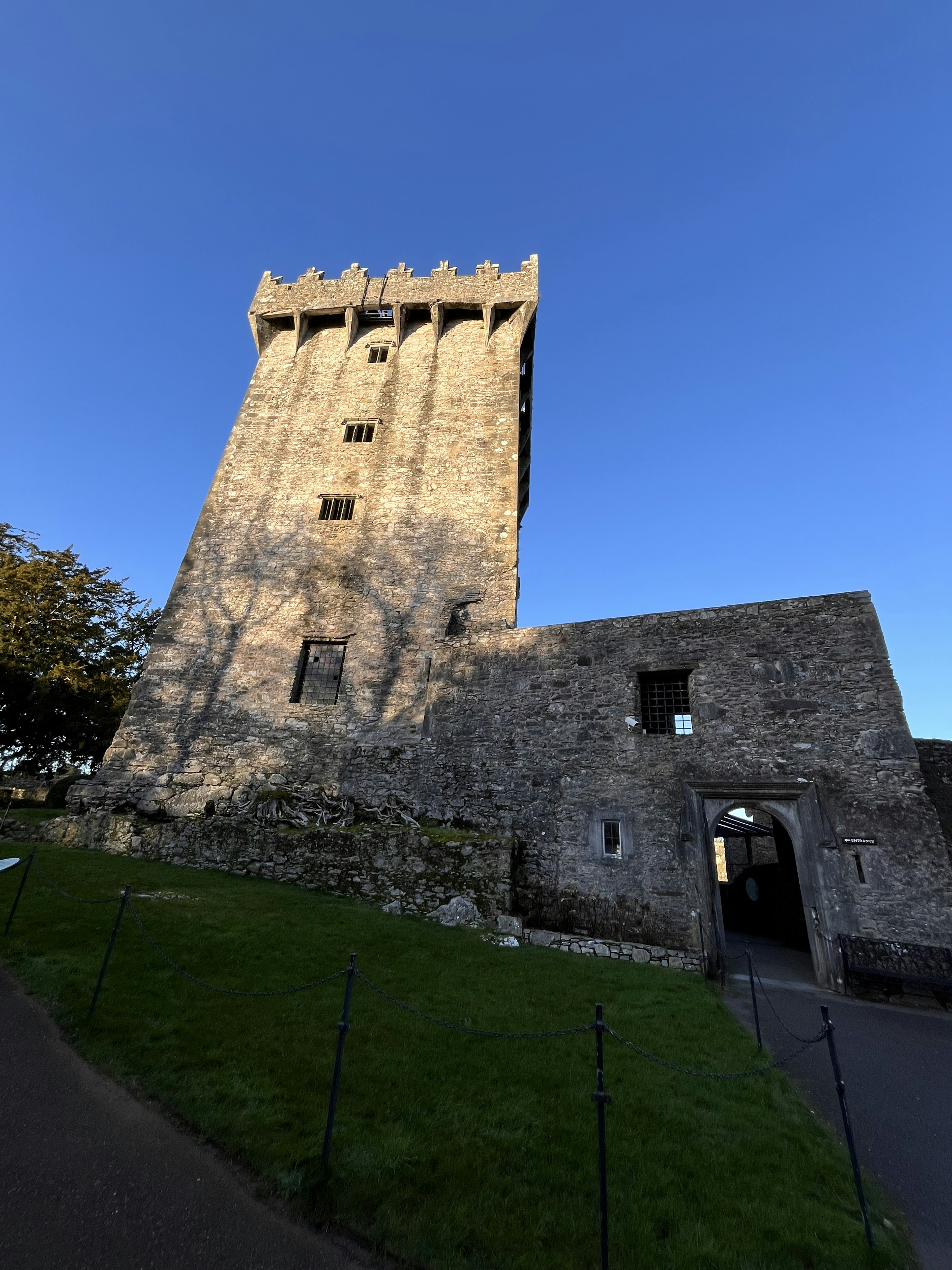 An ancient stone tower under a blue sky with remnants of a structure nearby