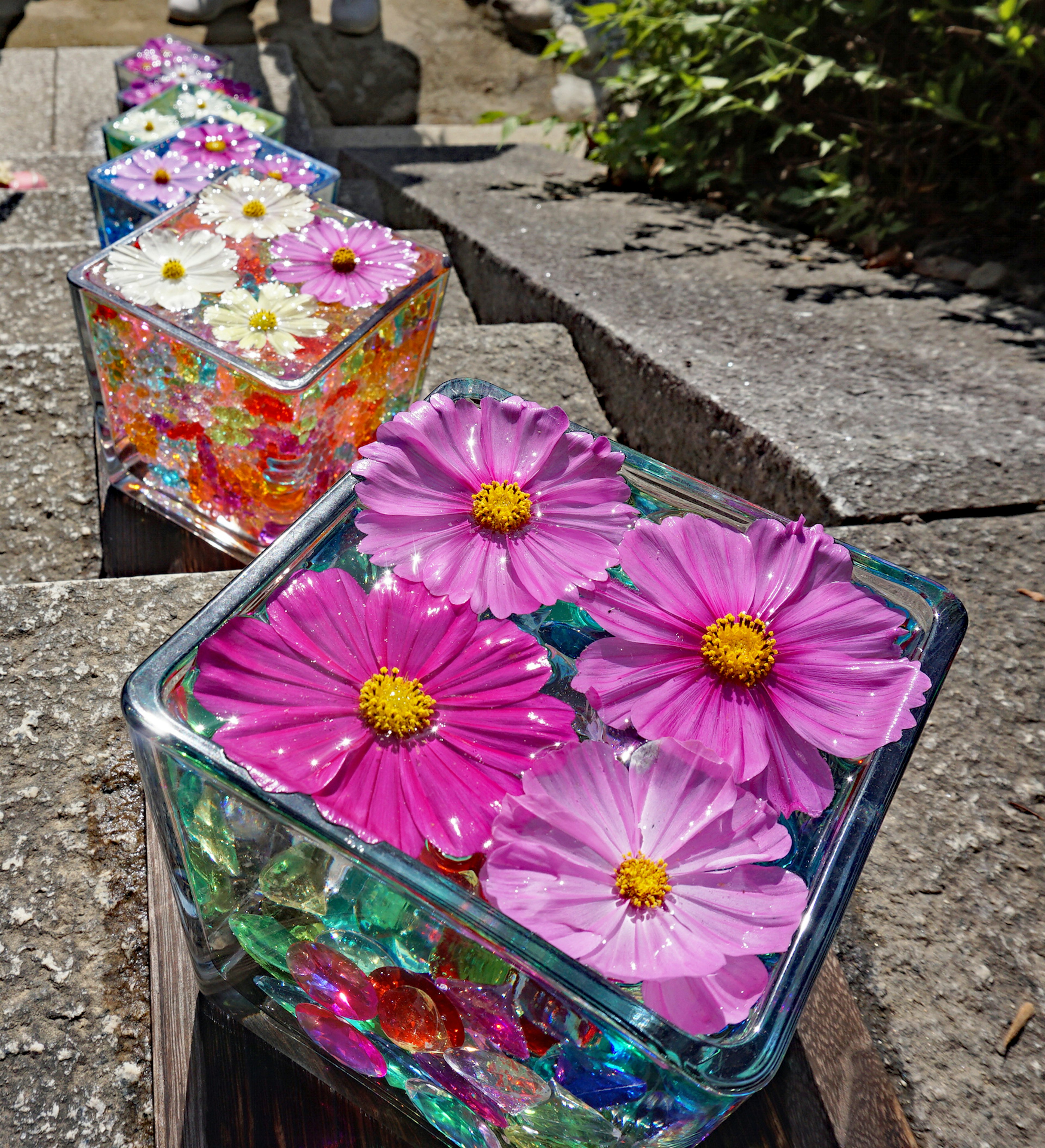 Fleurs colorées et perles dans des contenants transparents sur un chemin en pierre