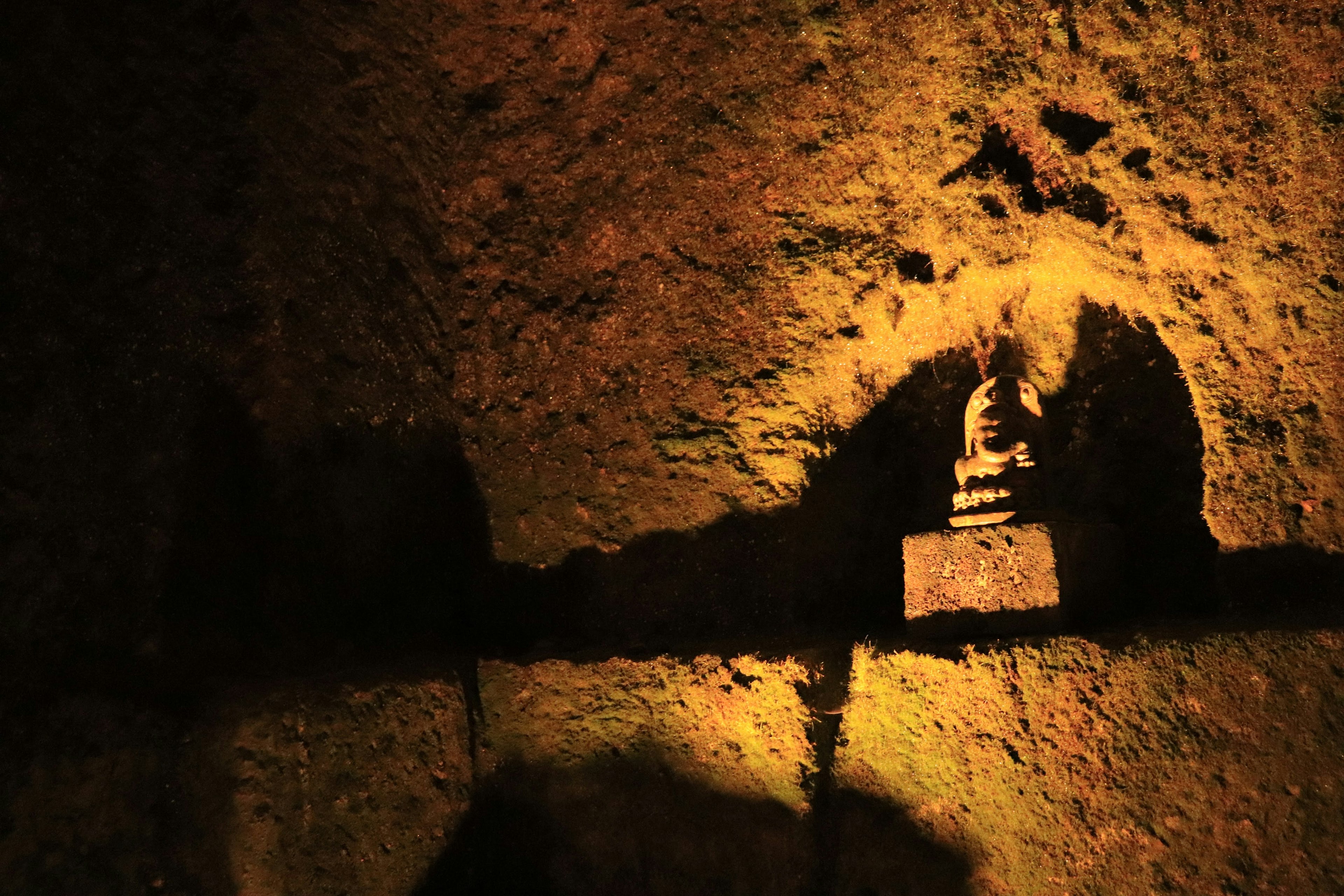 Silhouette d'une statue de Bouddha dans une grotte sombre éclairée par une lumière chaleureuse