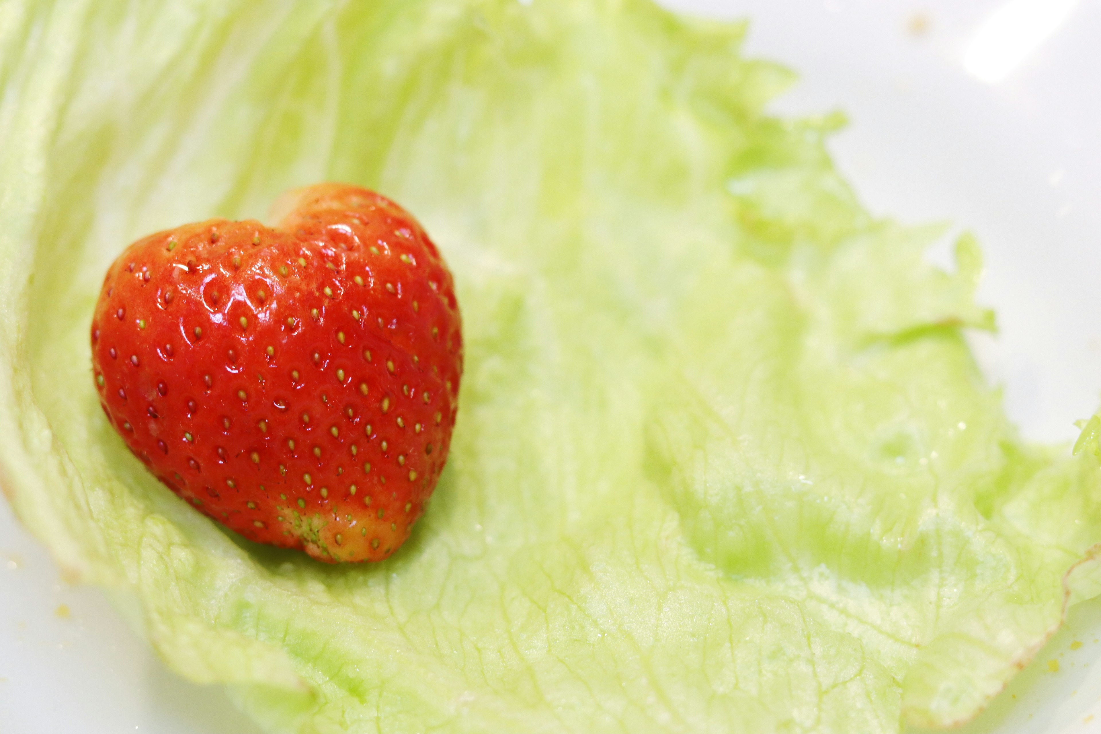 A heart-shaped strawberry placed on a green lettuce leaf