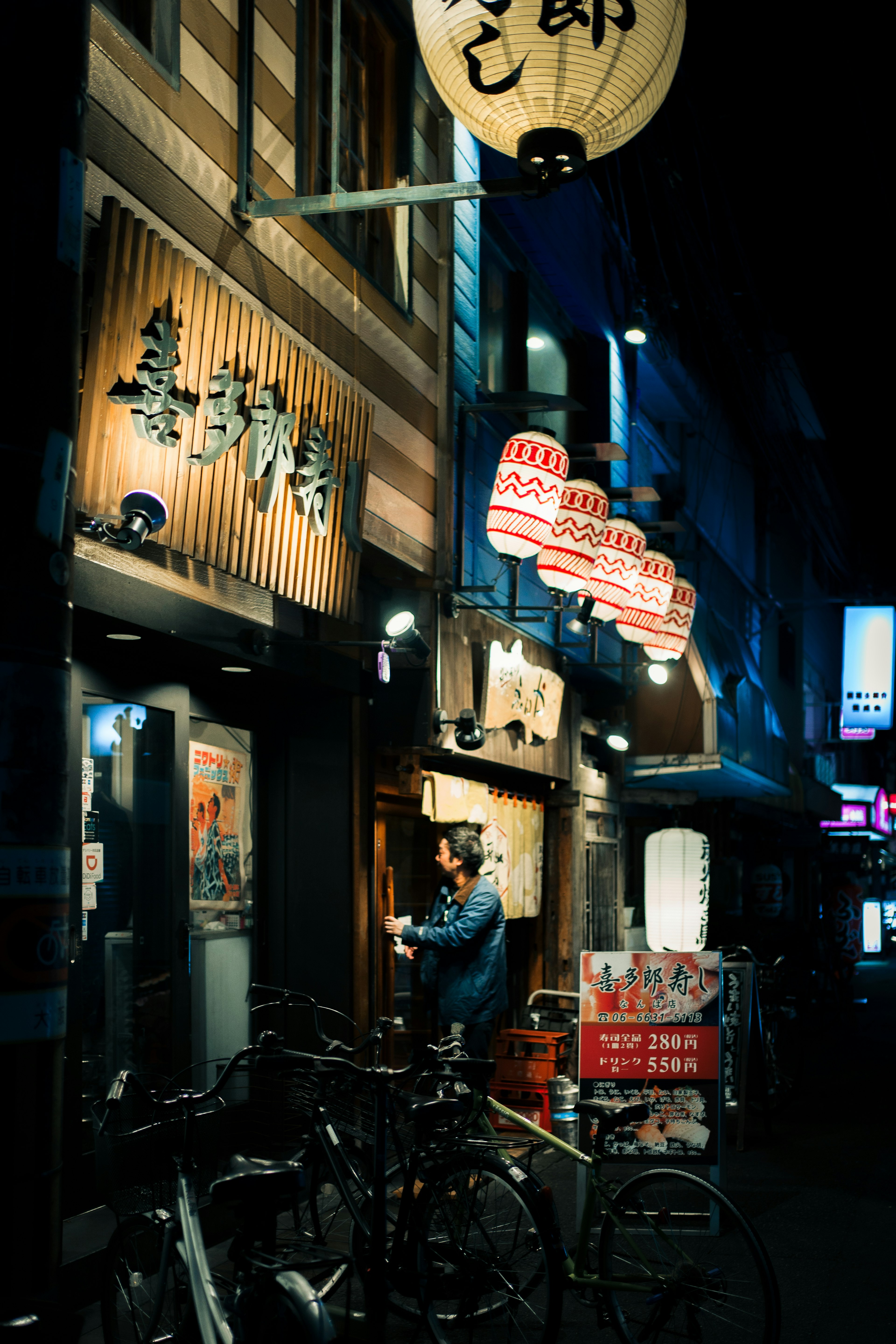 Exterior of a restaurant in a city at night bicycles parked illuminated signs and lanterns