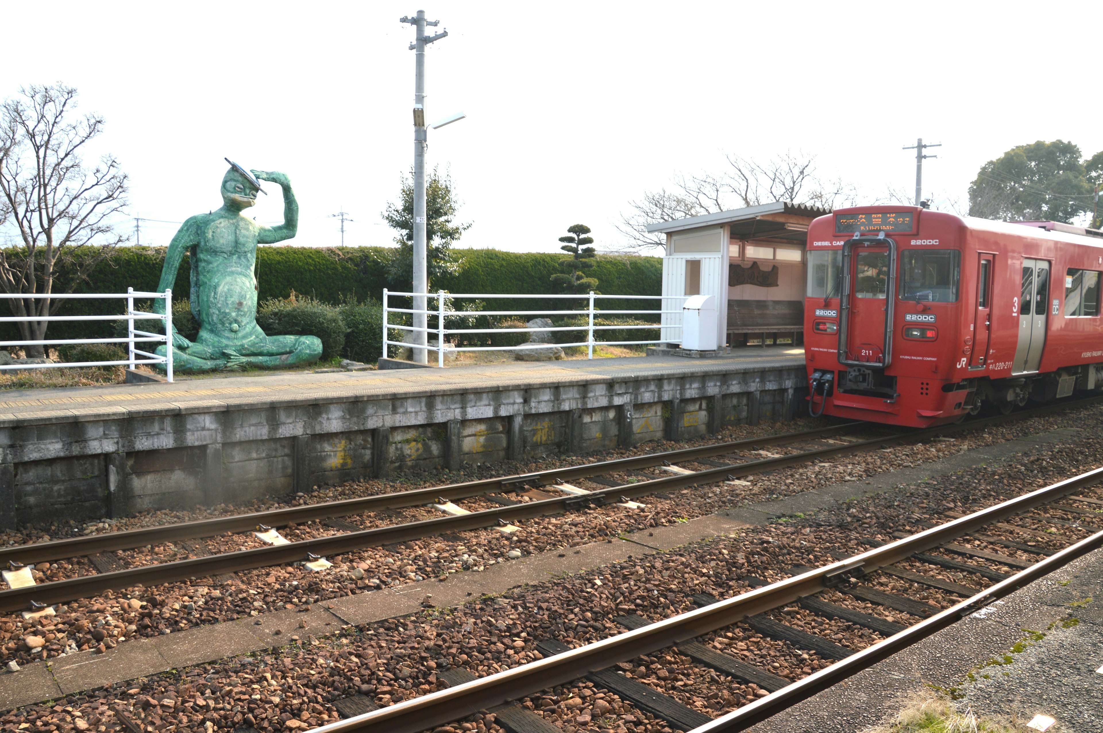 Un train rouge à une station avec une statue en bronze à proximité