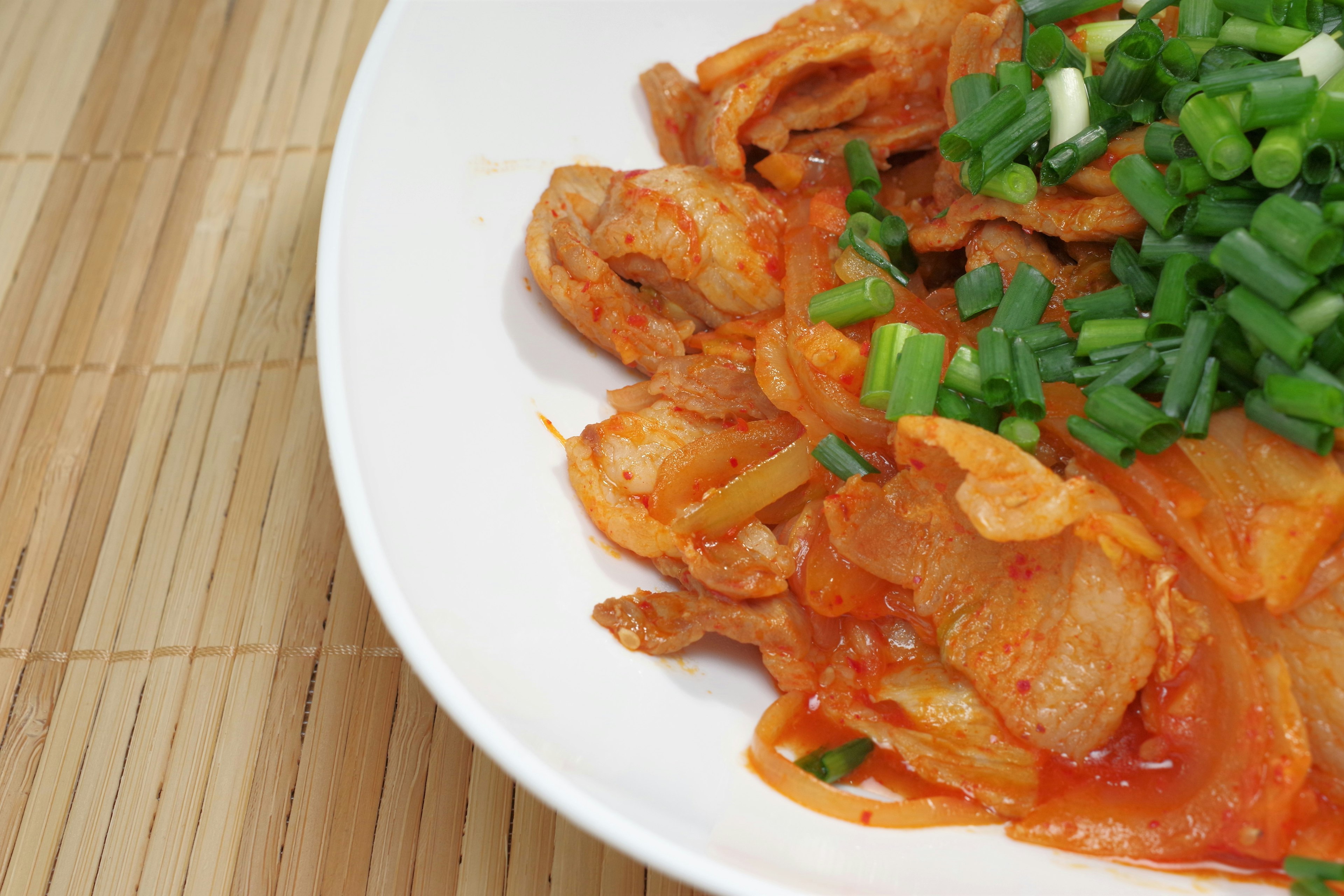 Un plato con kimchi rojo cubierto de cebollitas verdes