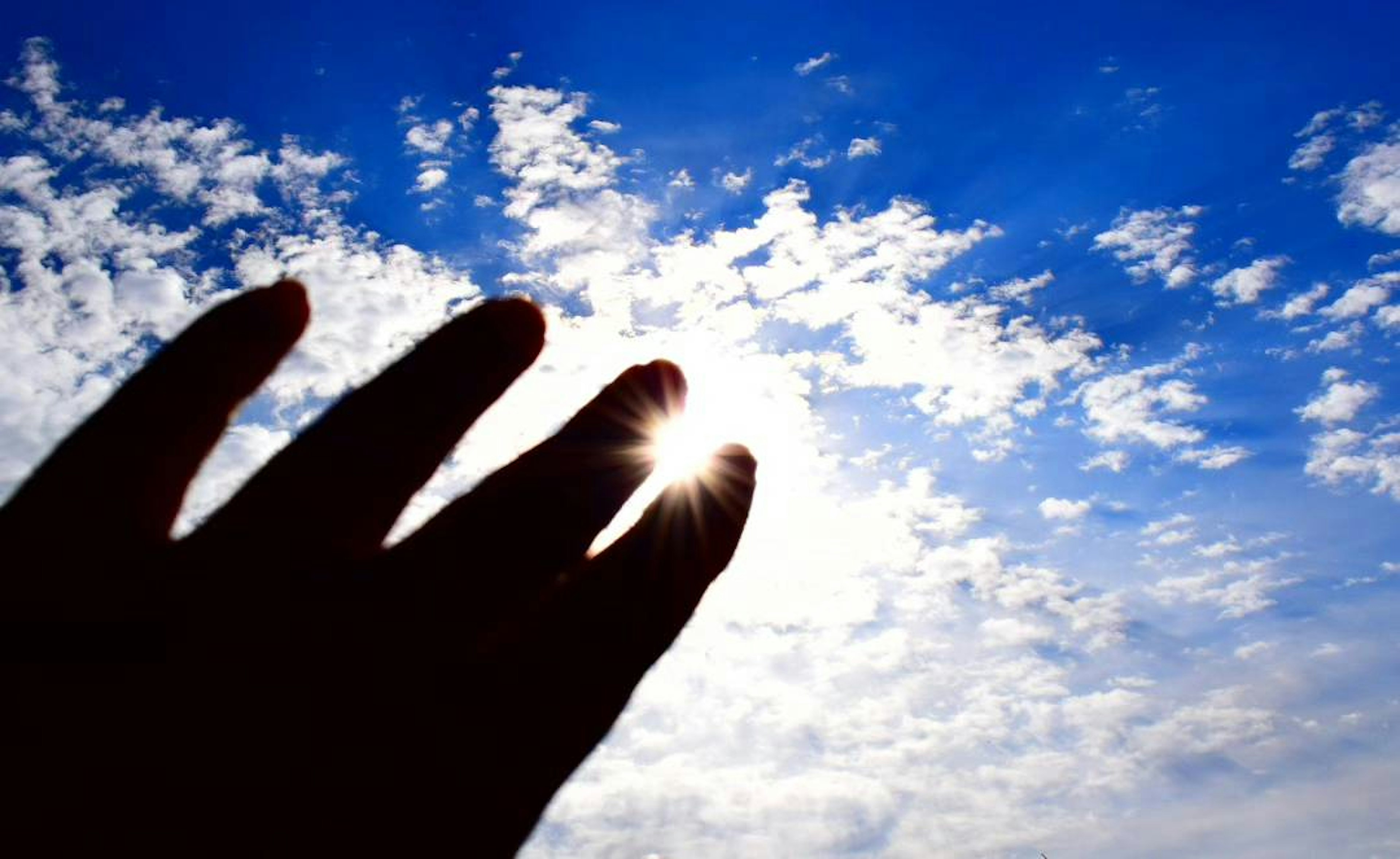 Silueta de una mano alcanzando el cielo azul