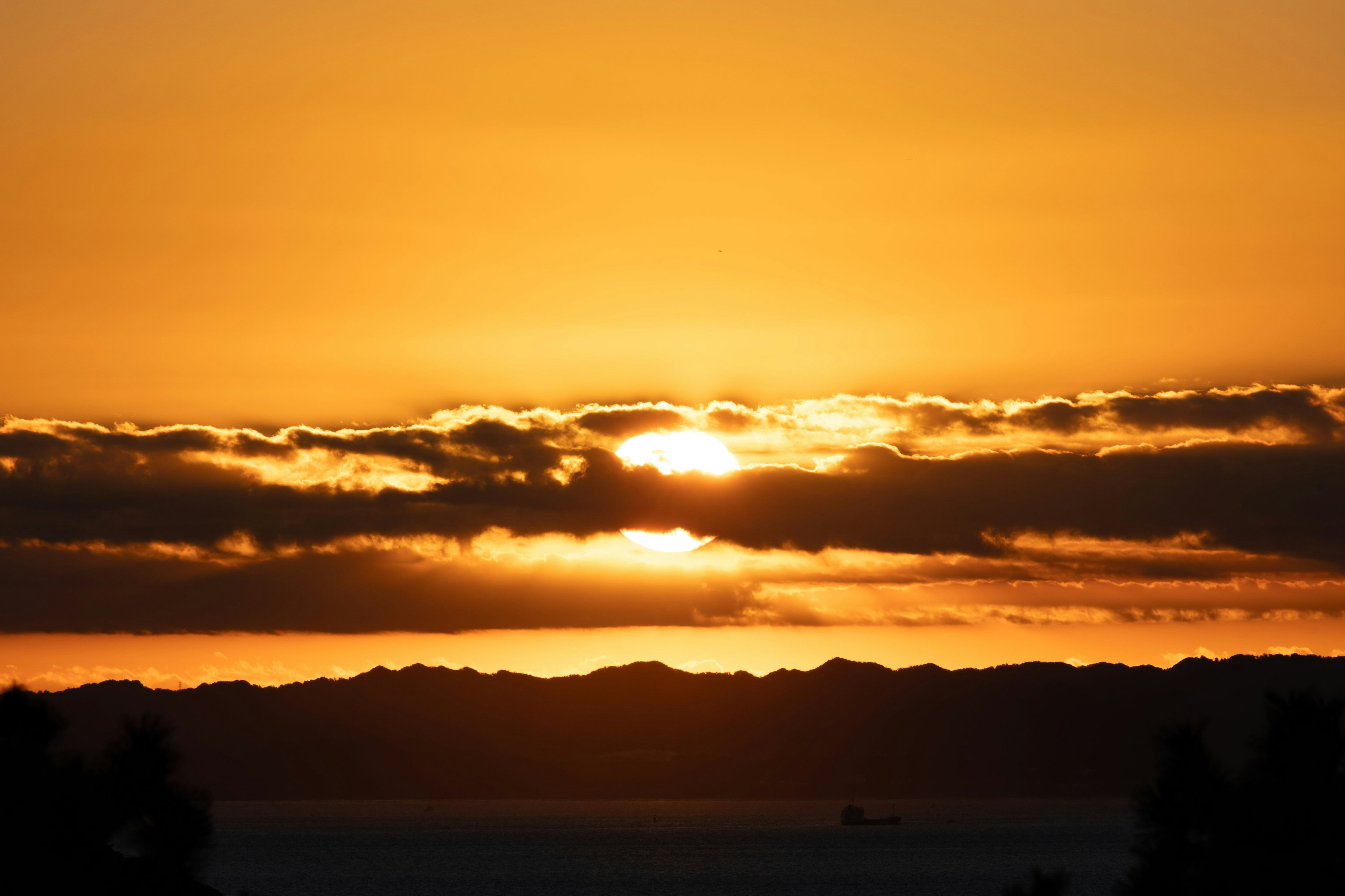 美しい夕日が雲の間から差し込む風景 海と山のシルエットが見える
