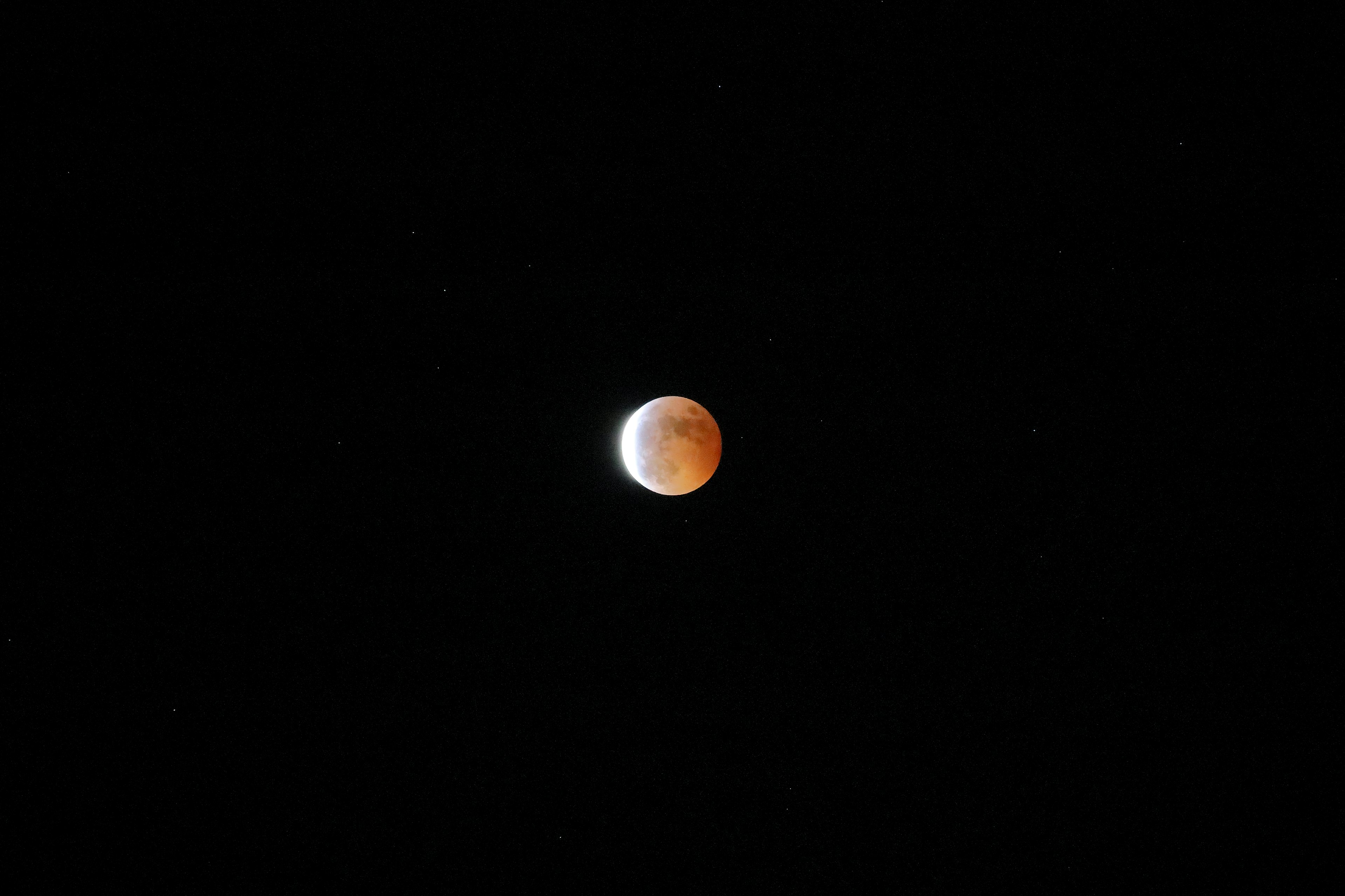 Éclipse partielle d'une lune rougeâtre dans le ciel nocturne