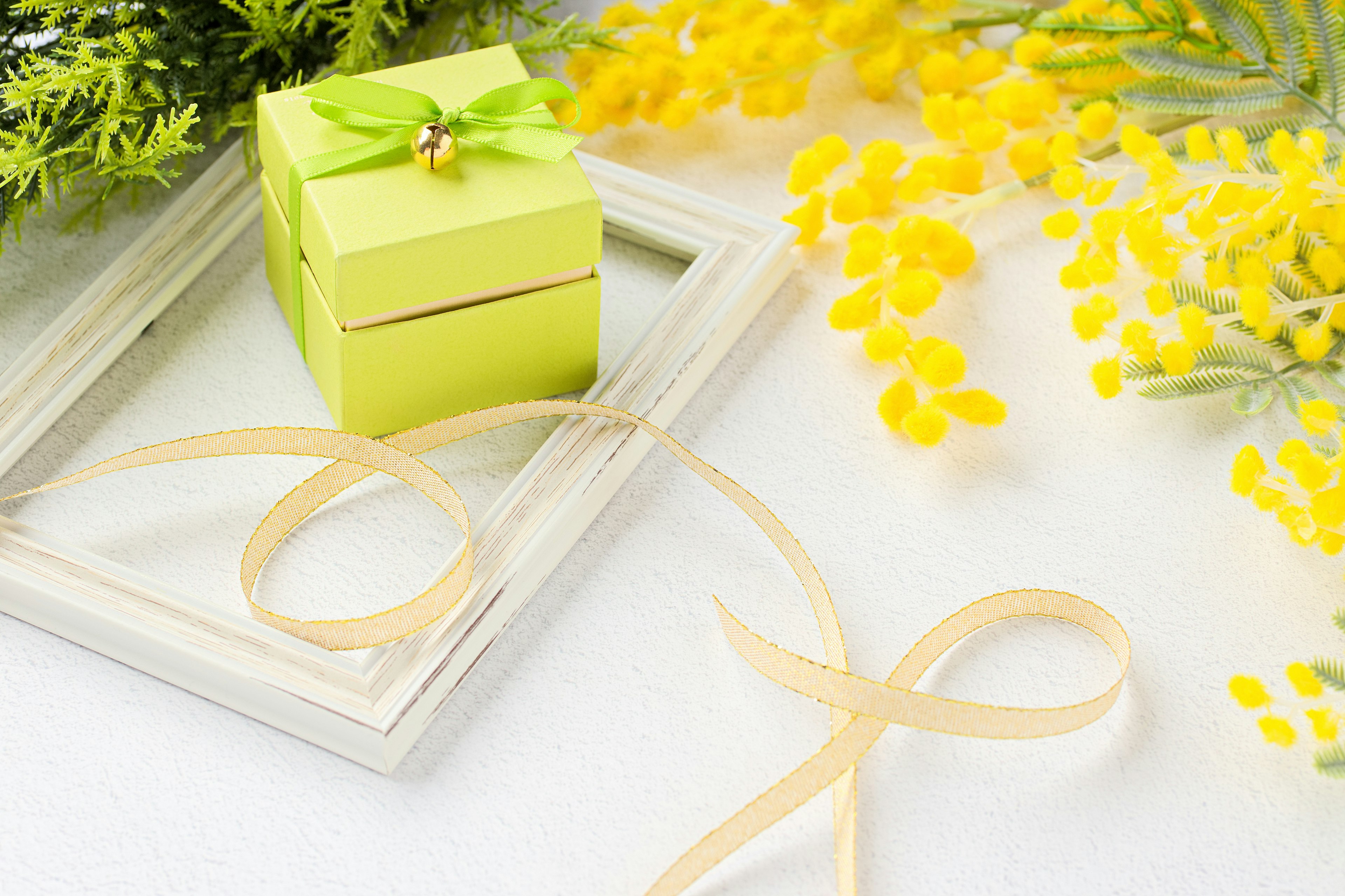 Image featuring a small green gift box surrounded by yellow mimosa flowers