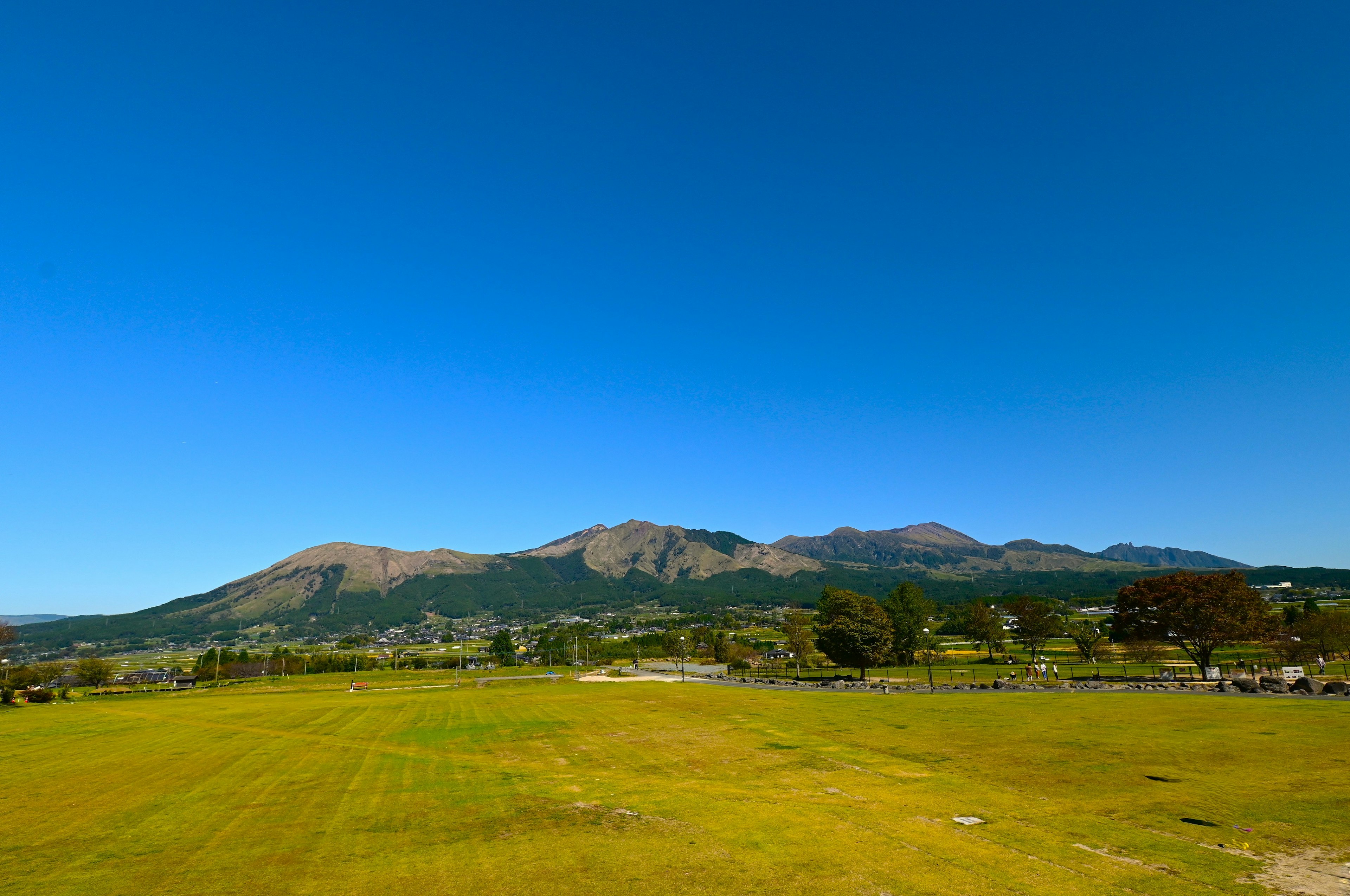 青空の下、広がる緑の草原と遠くの山々が見える風景