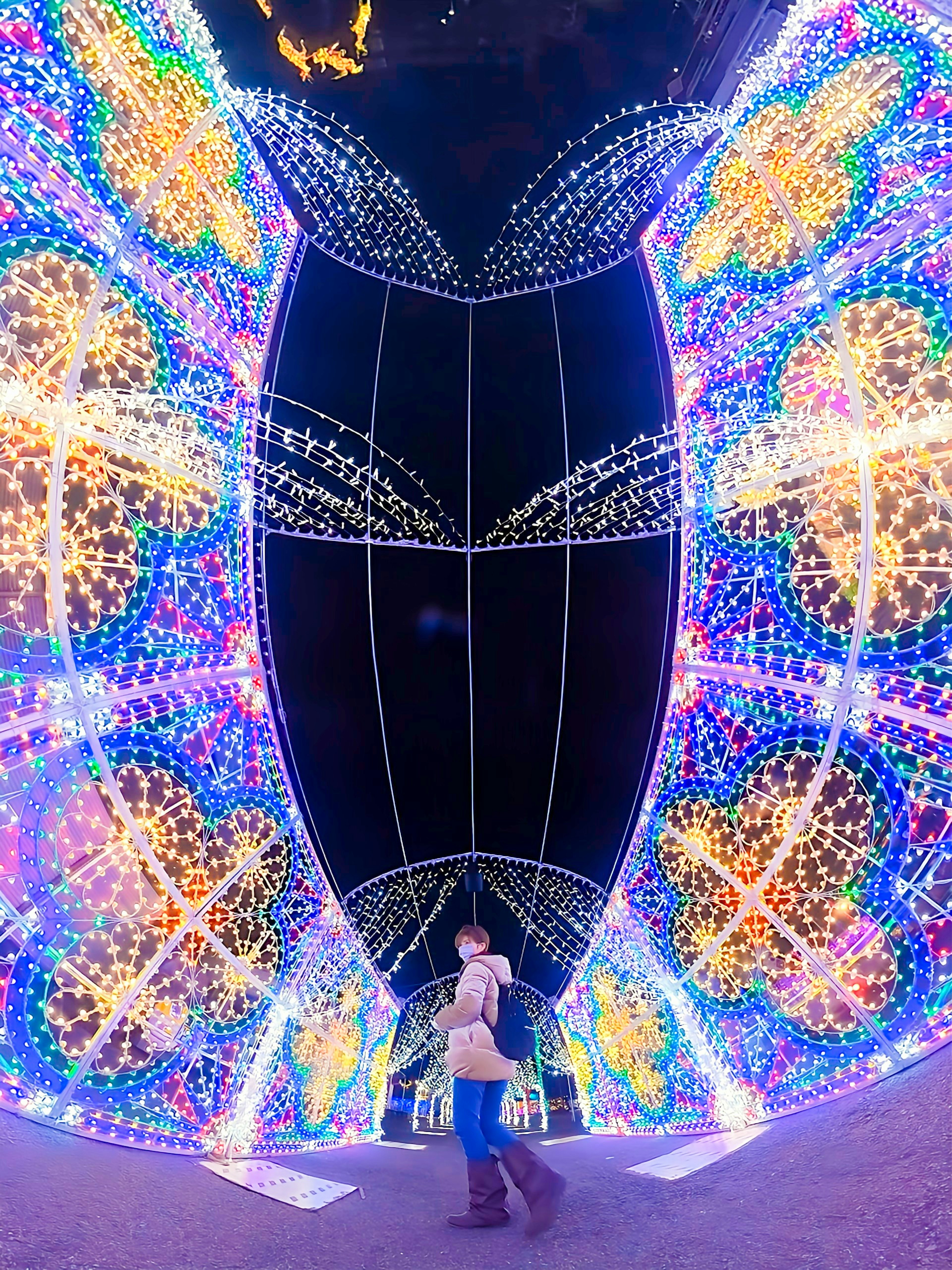 A woman standing under a beautifully decorated arch with colorful lights