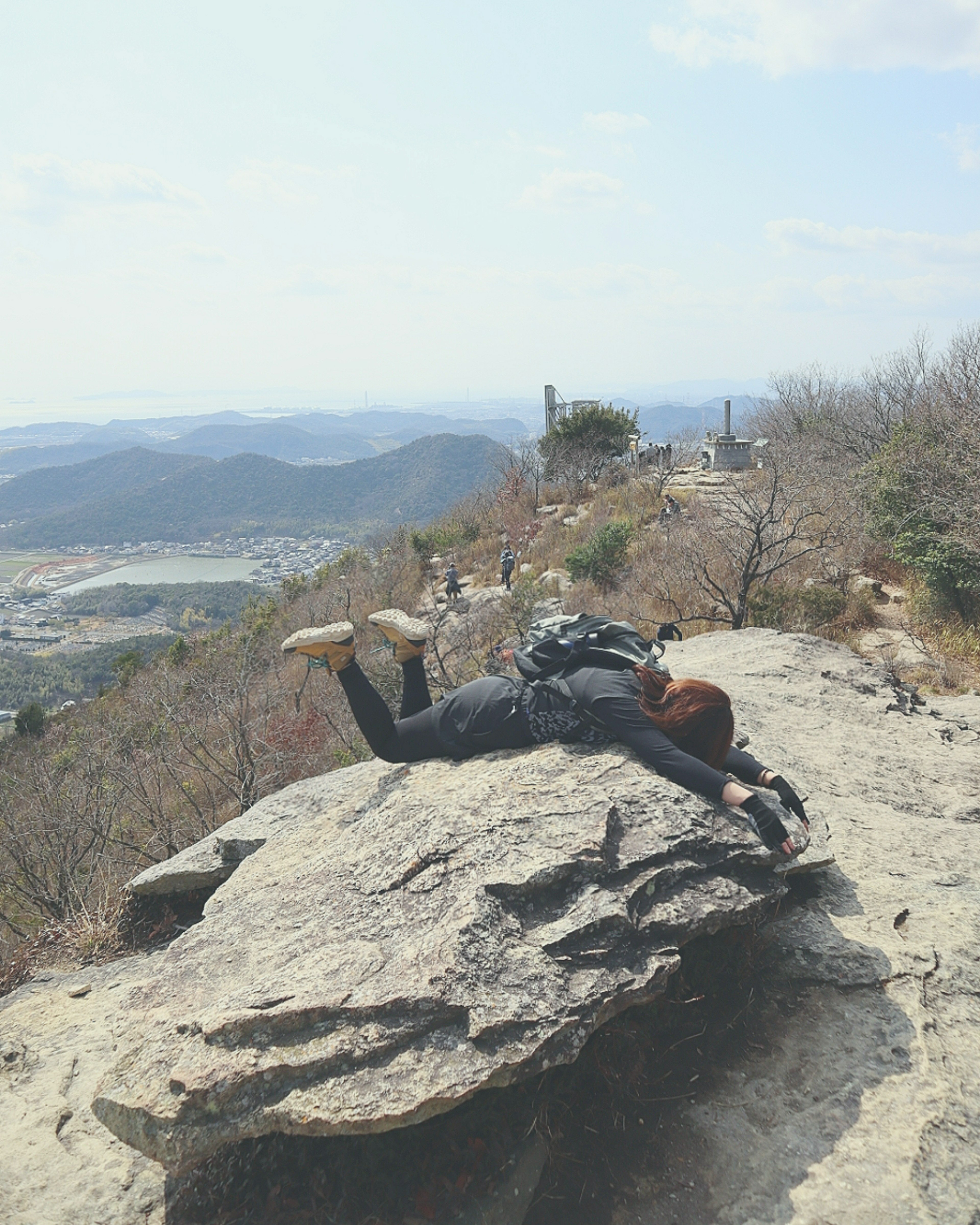 Hiker lying on a rock holding a camera with expansive mountain views