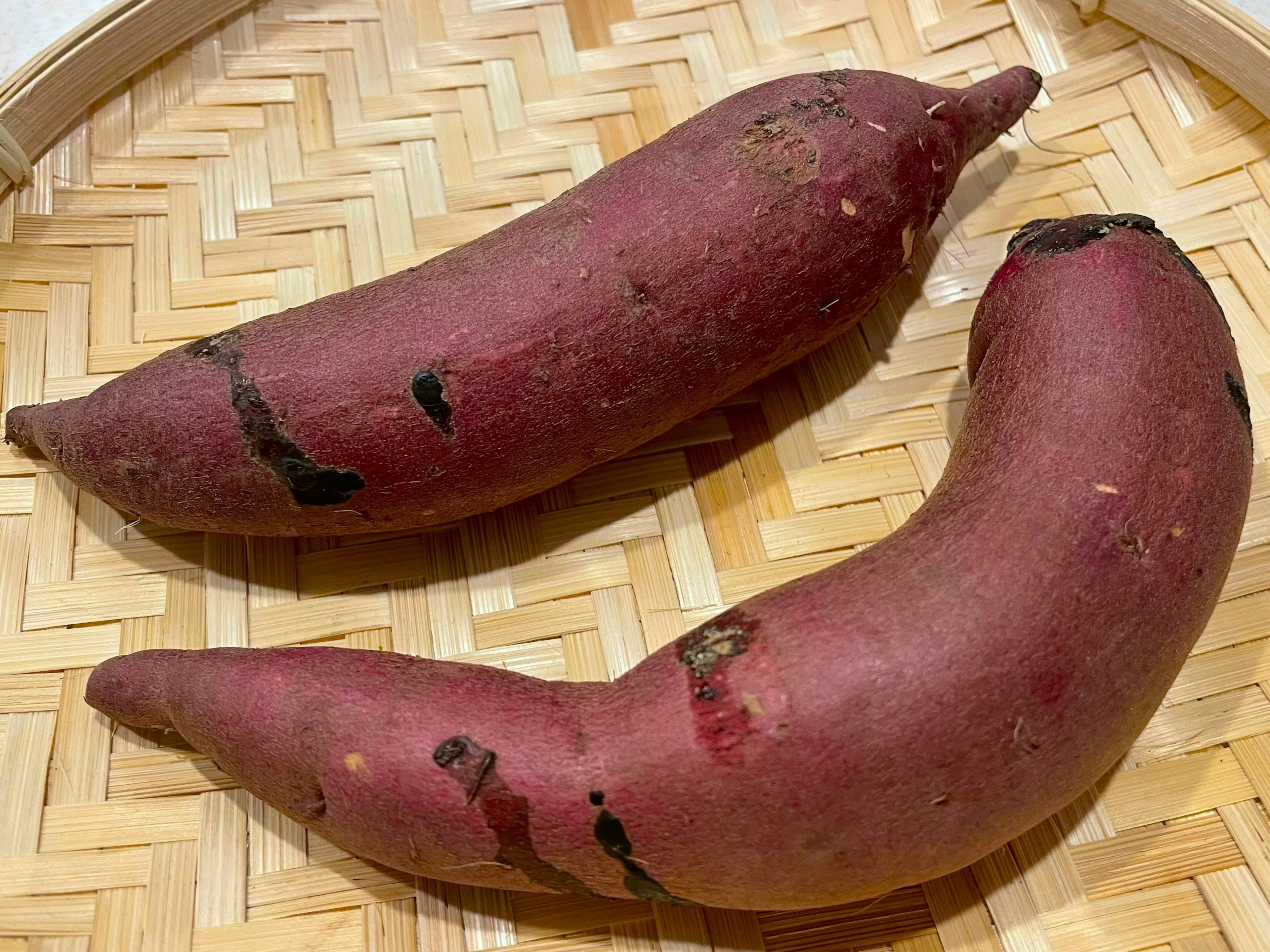 Two purple sweet potatoes placed on a woven basket