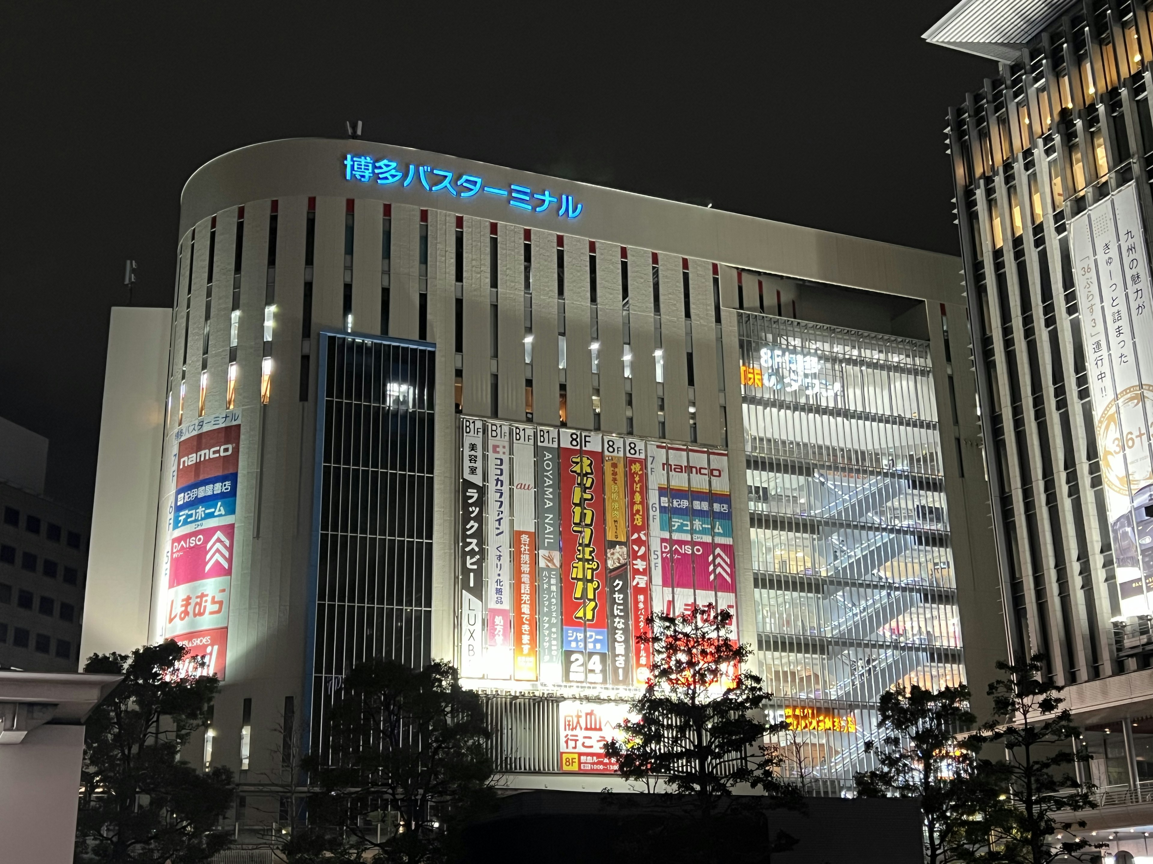 Vista nocturna del edificio de la estación de Hakata con letreros brillantes y arquitectura moderna