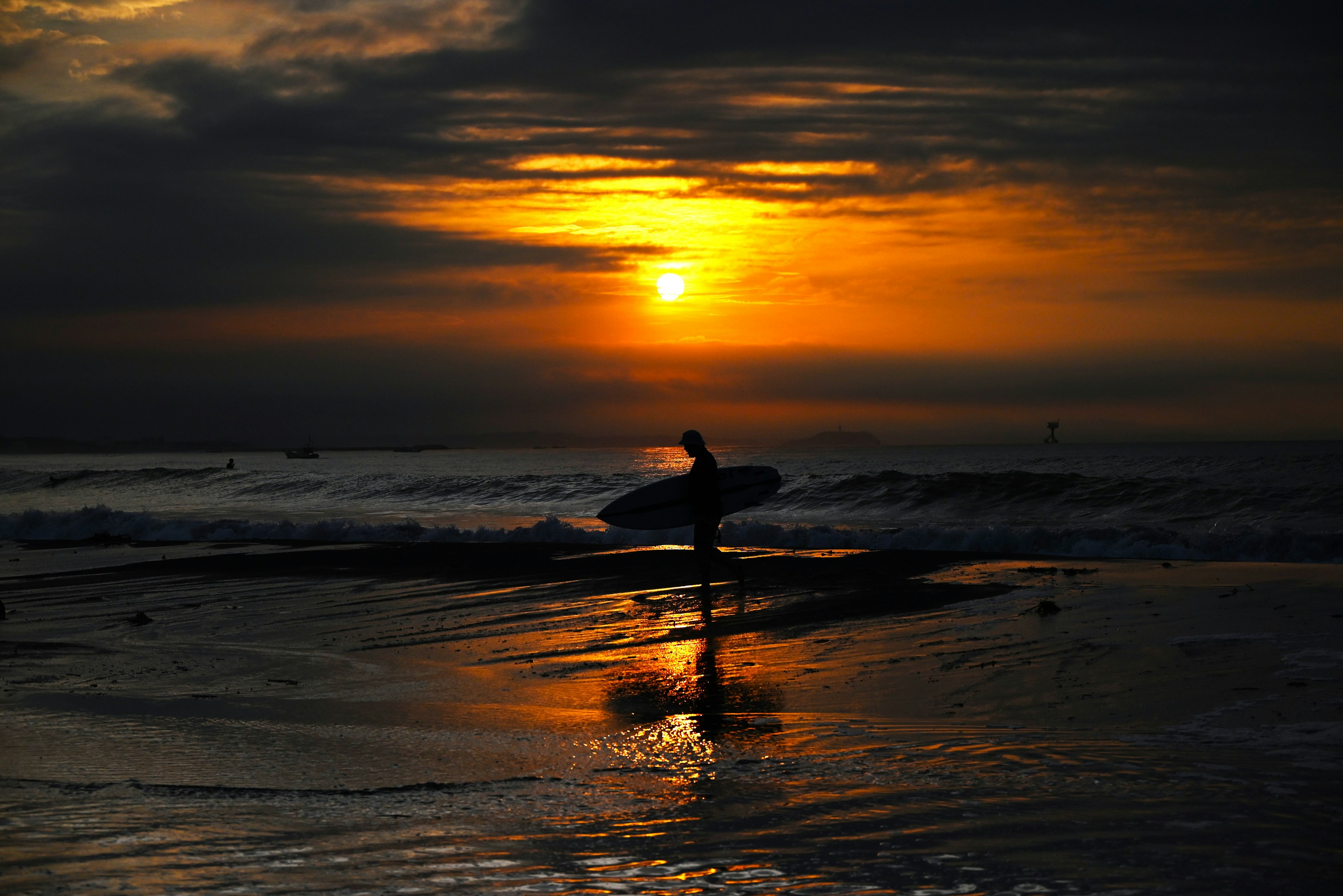 サーフィンをする人が夕日を背にしているビーチの風景