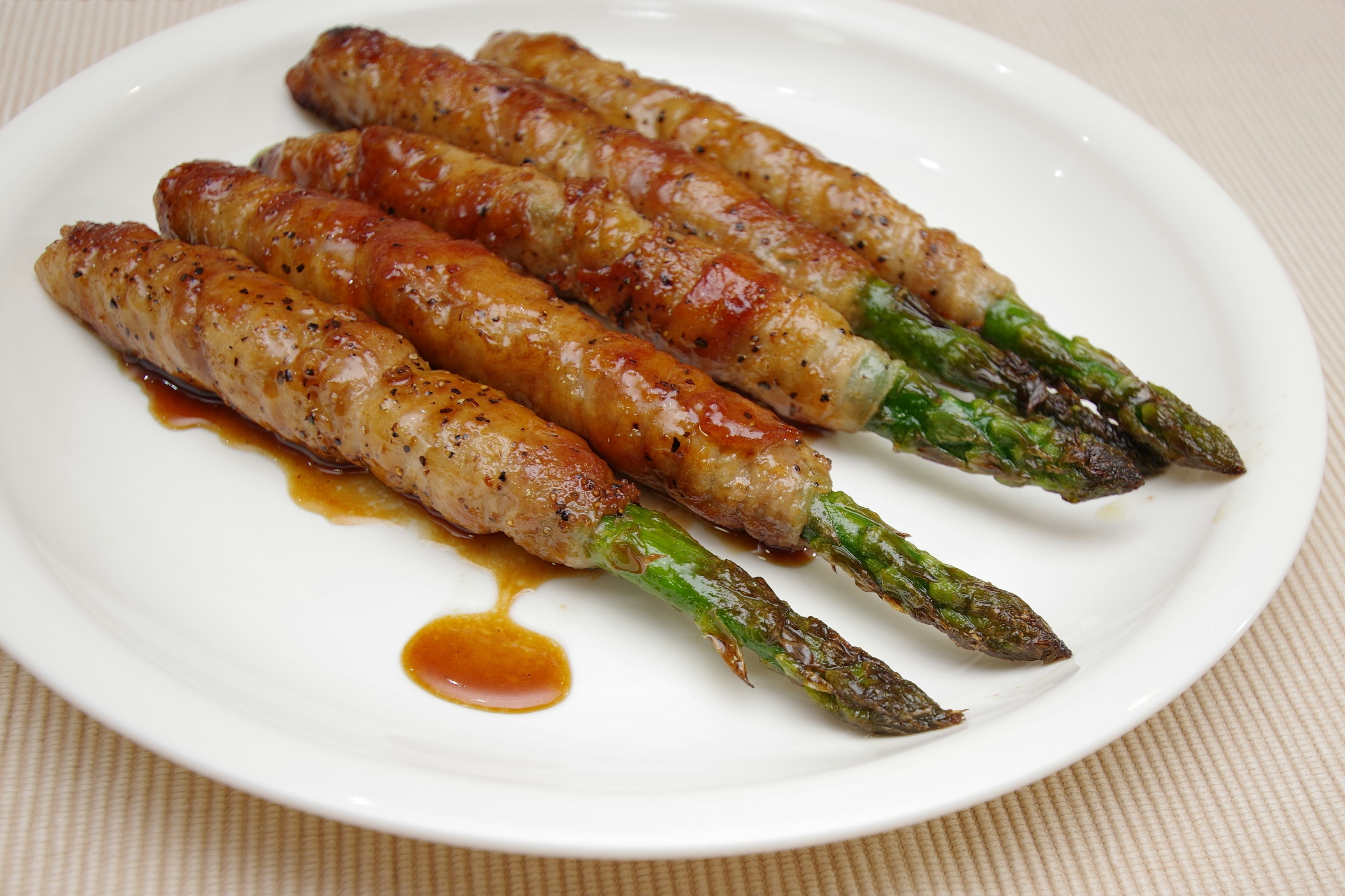 Gegrillte Spargel umwickelt mit Fleisch auf einem weißen Teller serviert