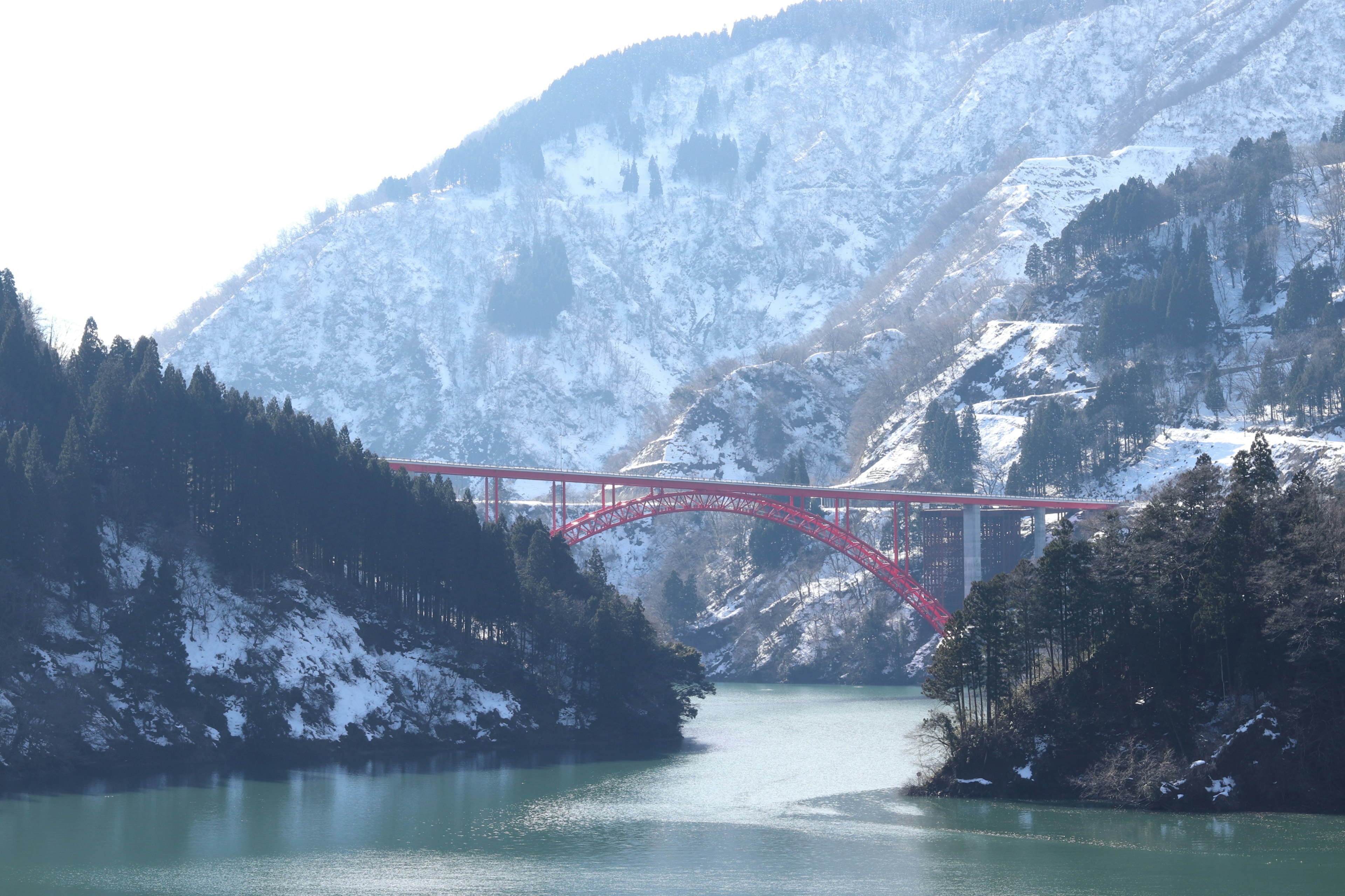 雪覆蓋的山脈與橫跨湖泊的紅色橋樑的風景