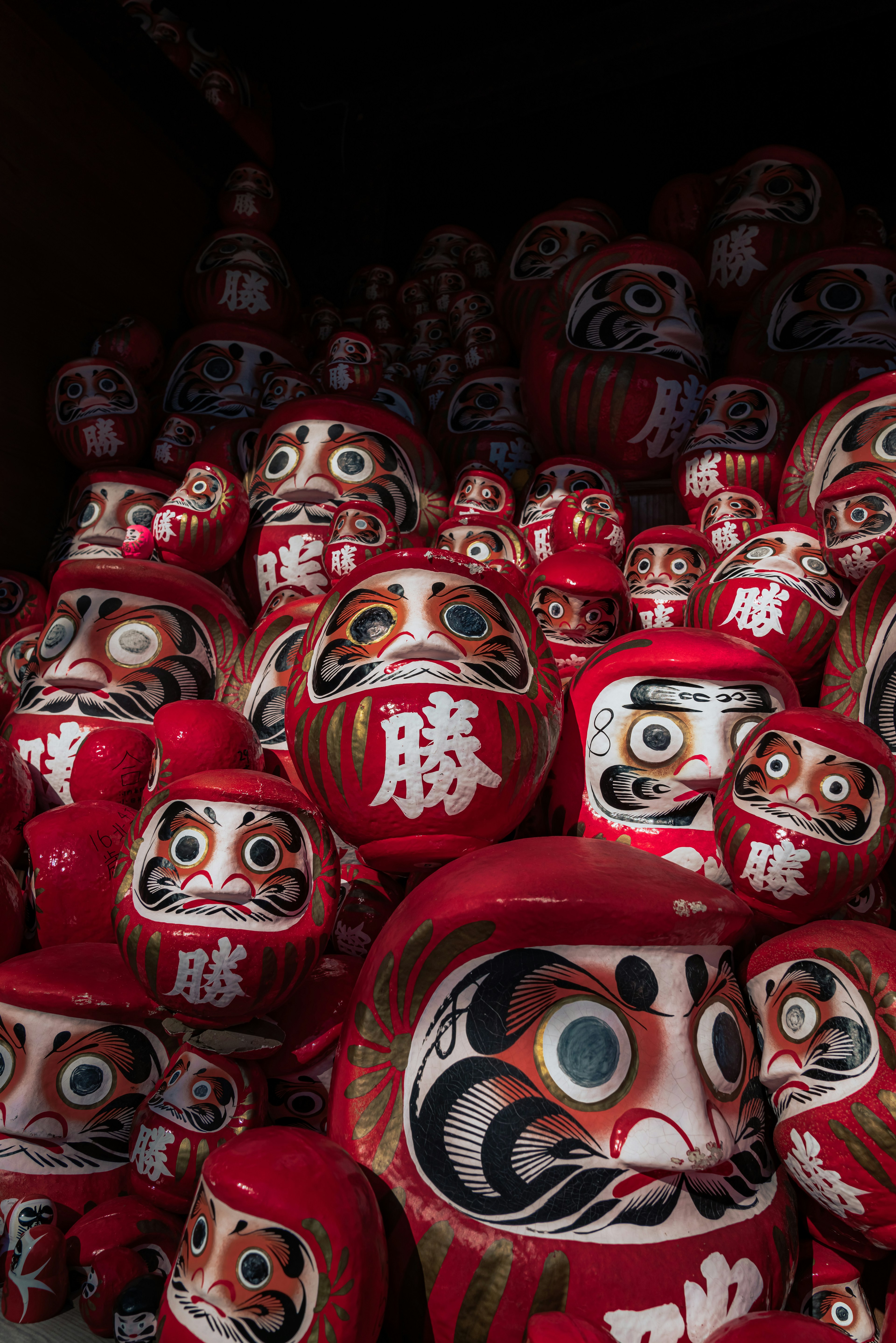 Sekumpulan boneka Daruma merah yang ditumpuk dengan fitur wajah unik