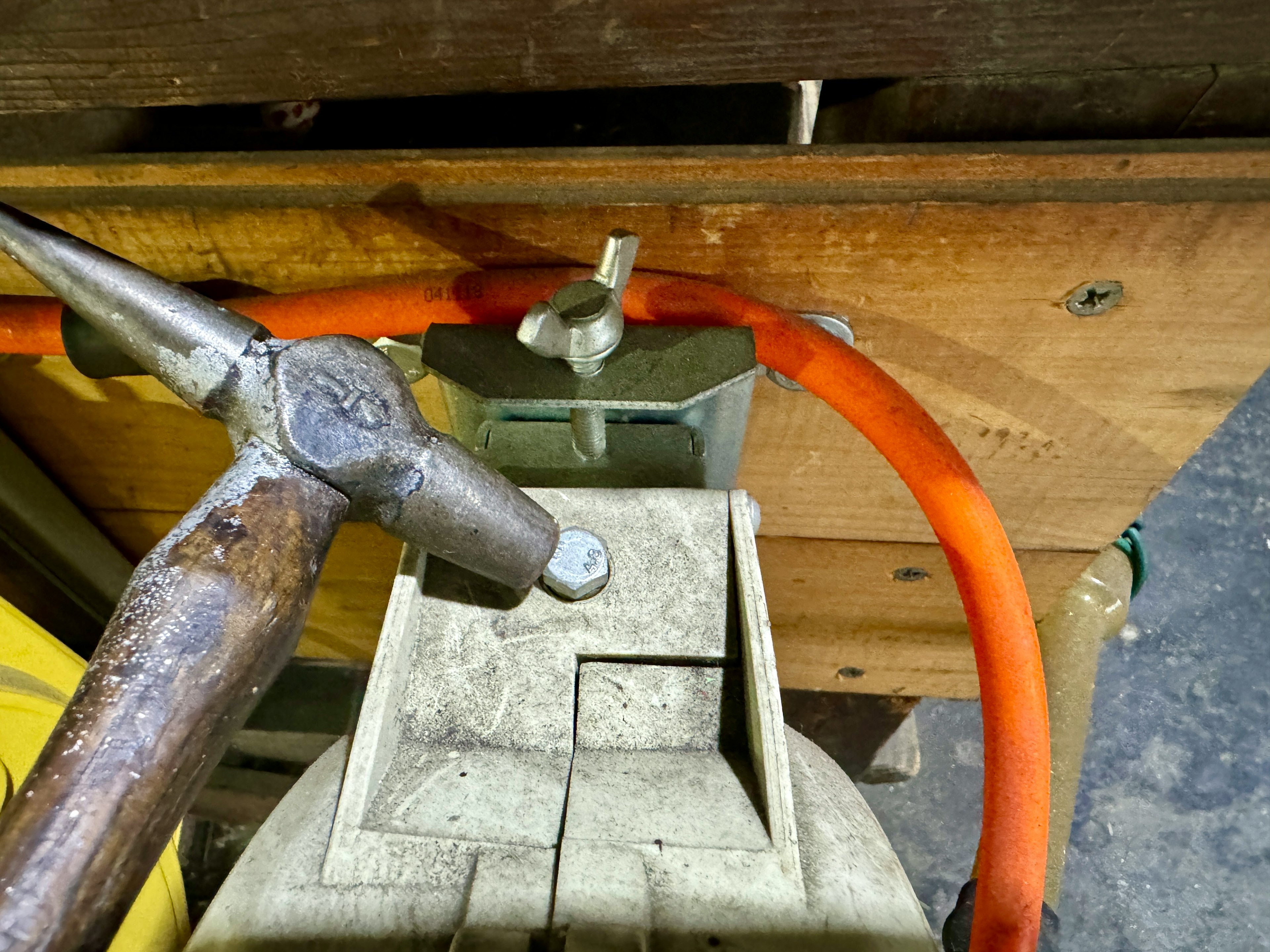 La imagen muestra una conexión de herramienta y manguera en un banco de trabajo de madera