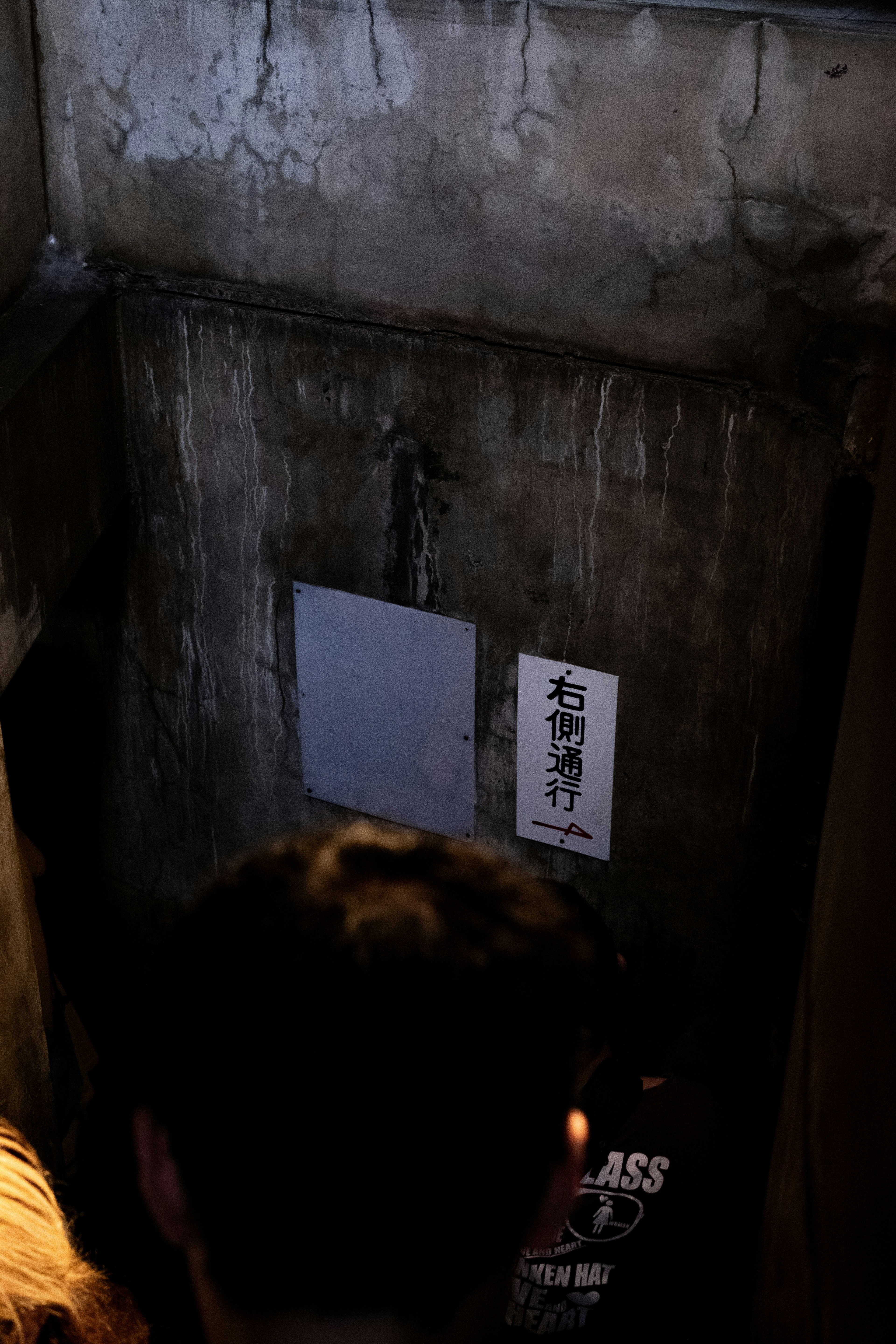 Escalier faiblement éclairé menant à un mur usé avec une signalisation japonaise