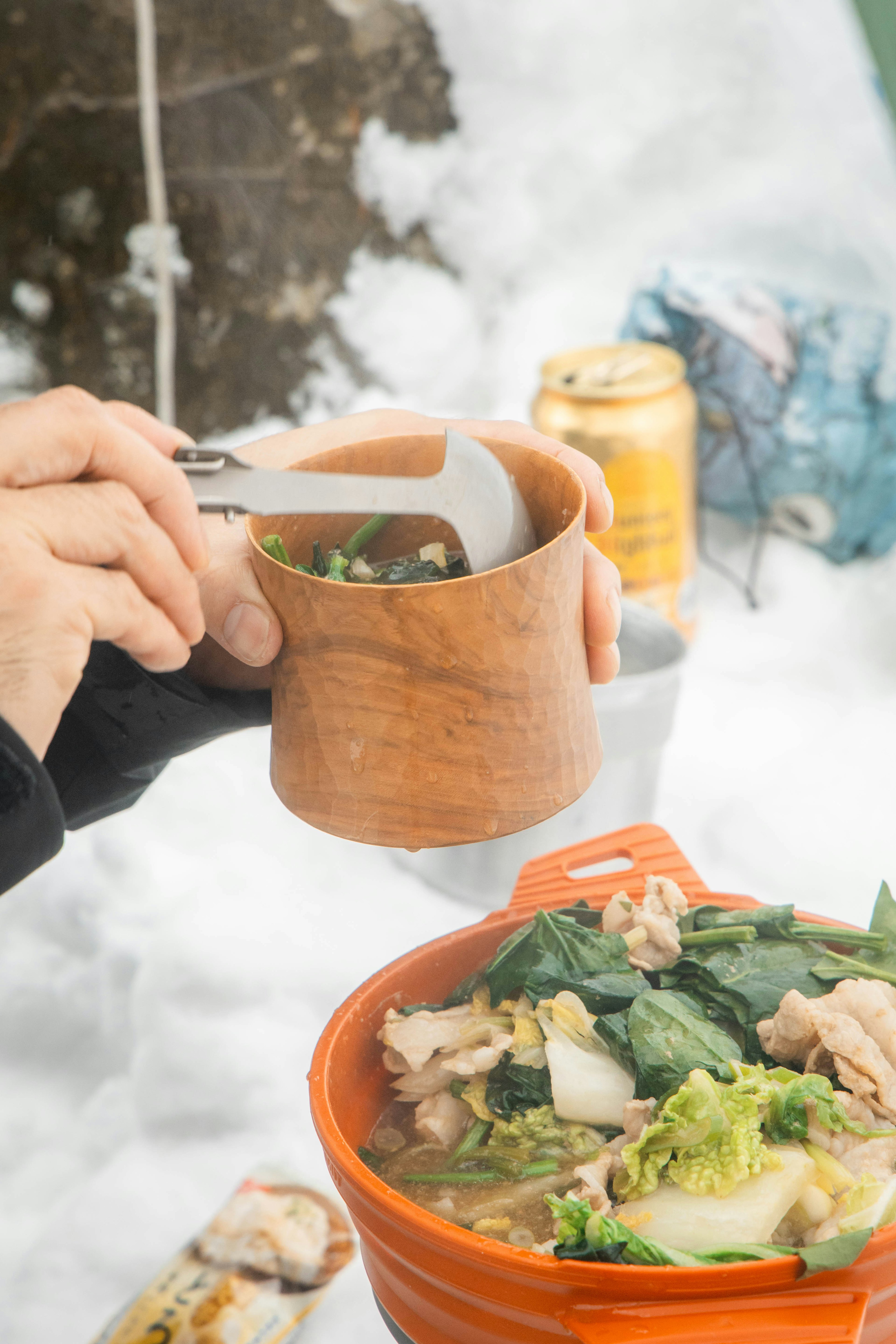 Hand hält eine Holztasse während sie Suppe im Schnee genießen