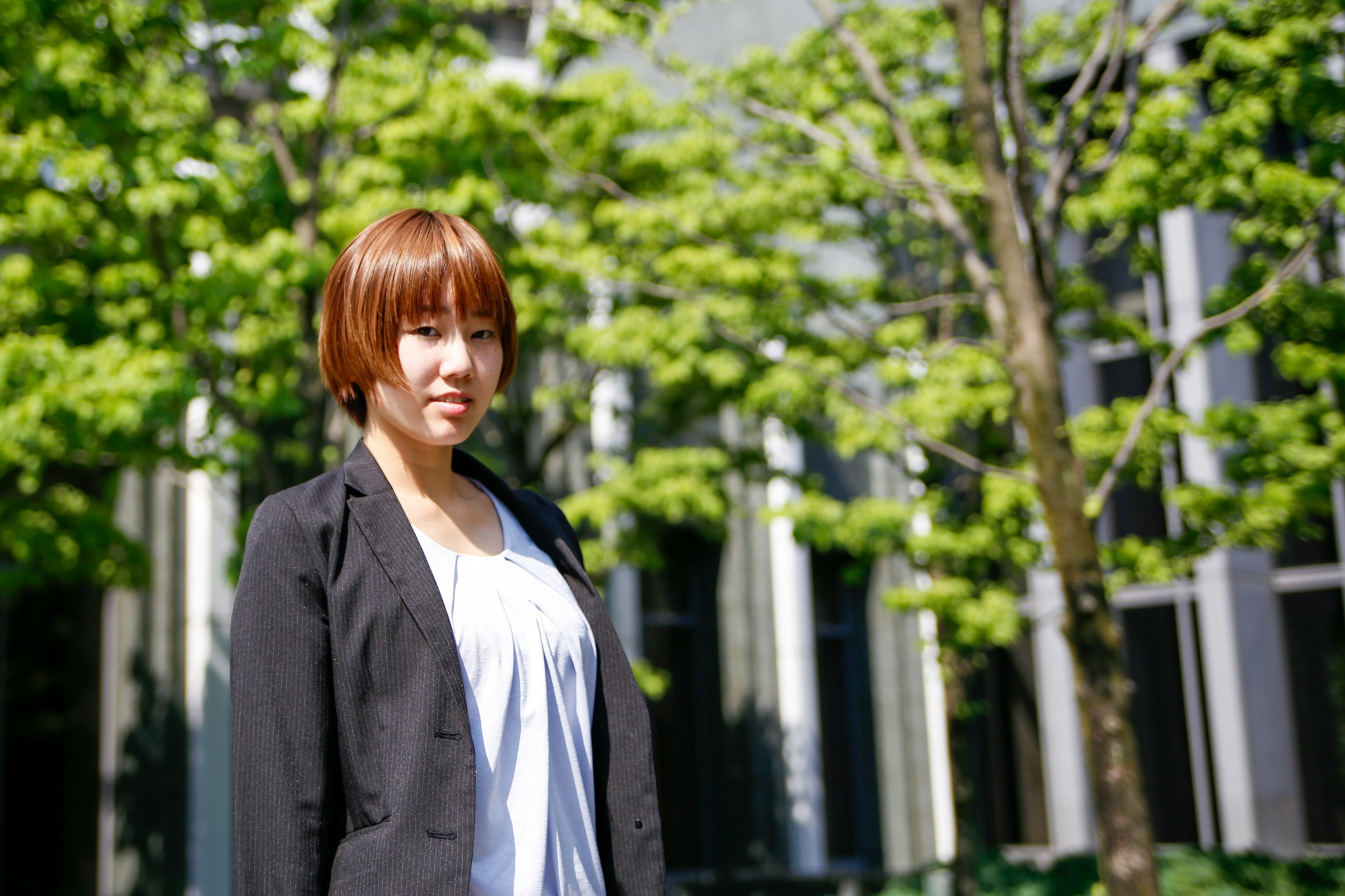 Portrait of a woman standing in front of green trees with short hair and wearing a suit