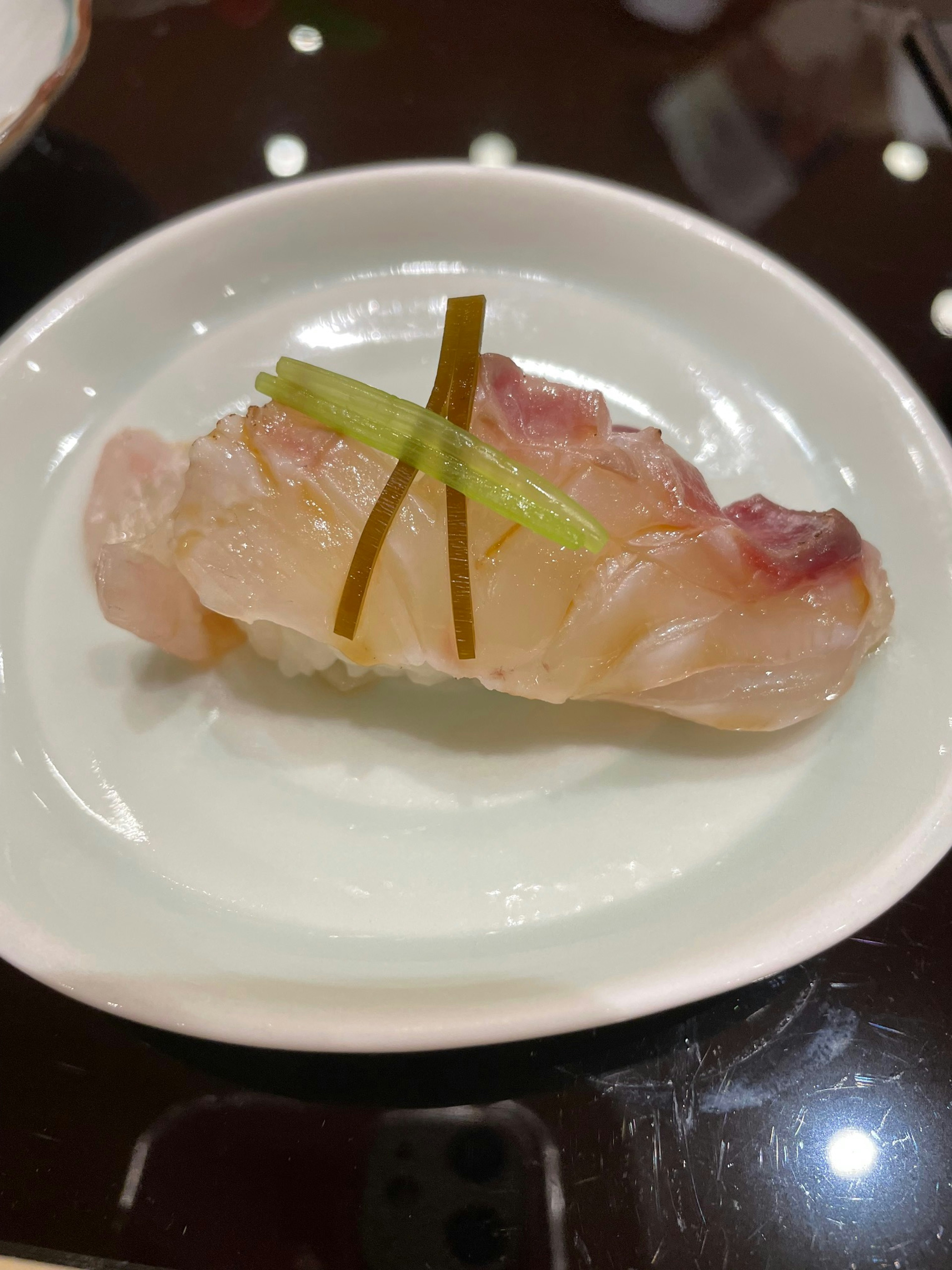 Trozo de sushi con pescado blanco cubierto con cebolla verde y alga