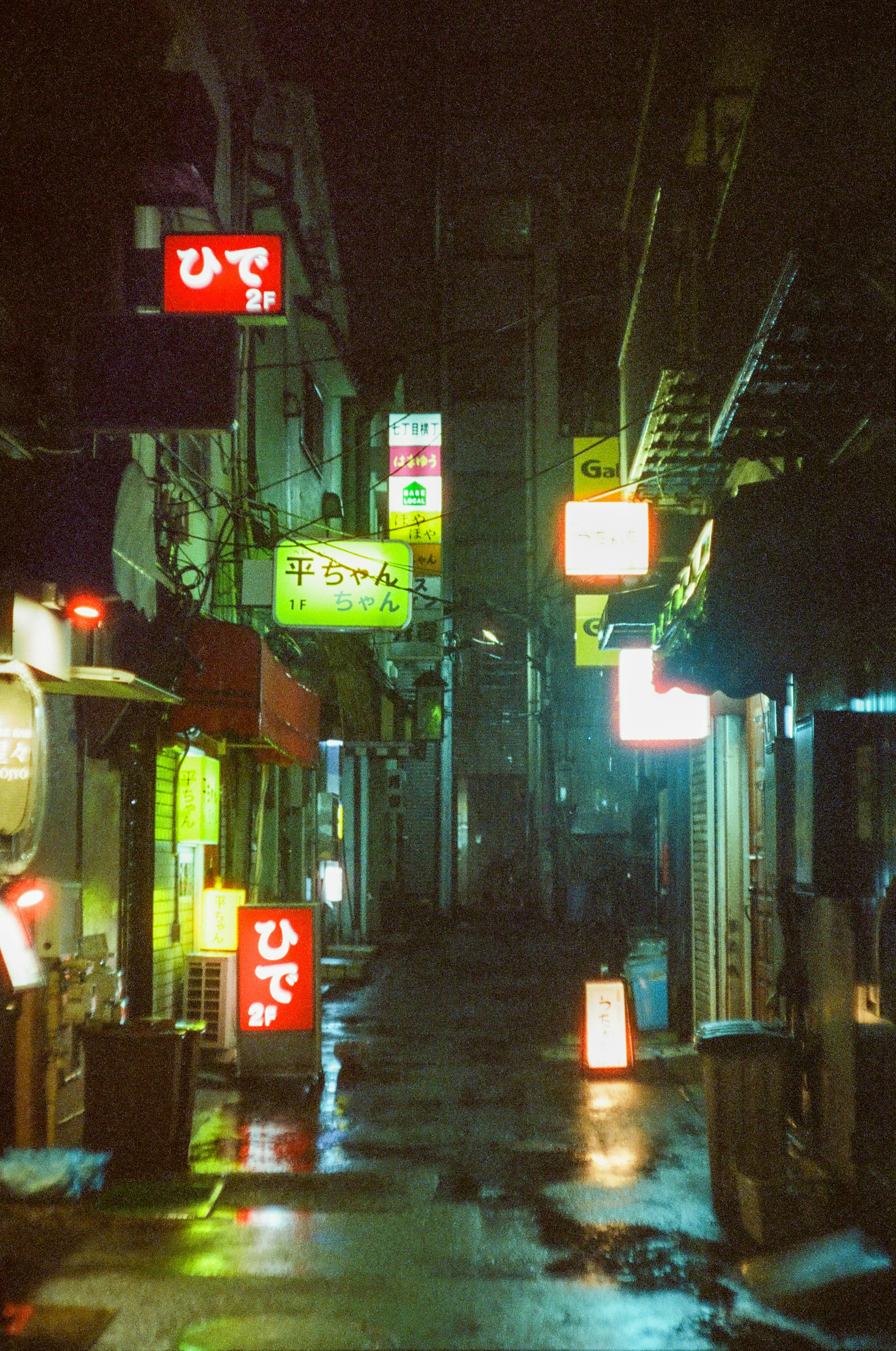 Narrow alley illuminated by neon signs and wet pavement at night