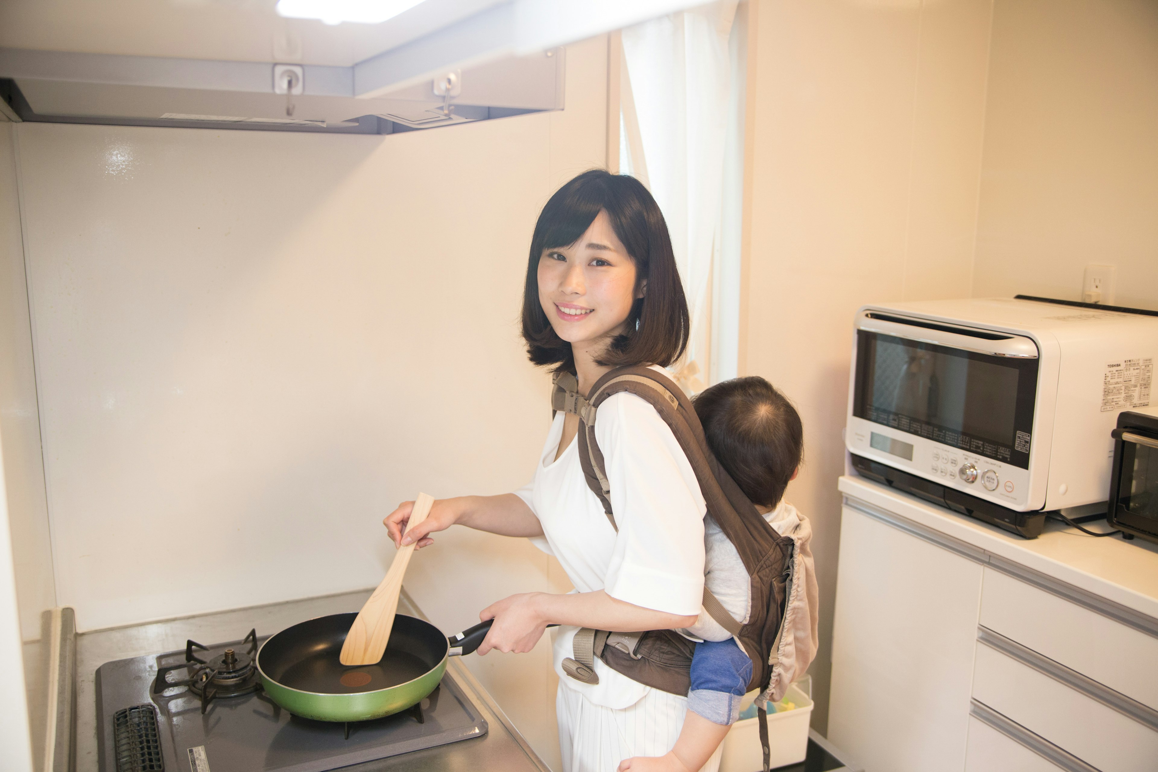 Madre cocinando en una cocina con un bebé en la espalda