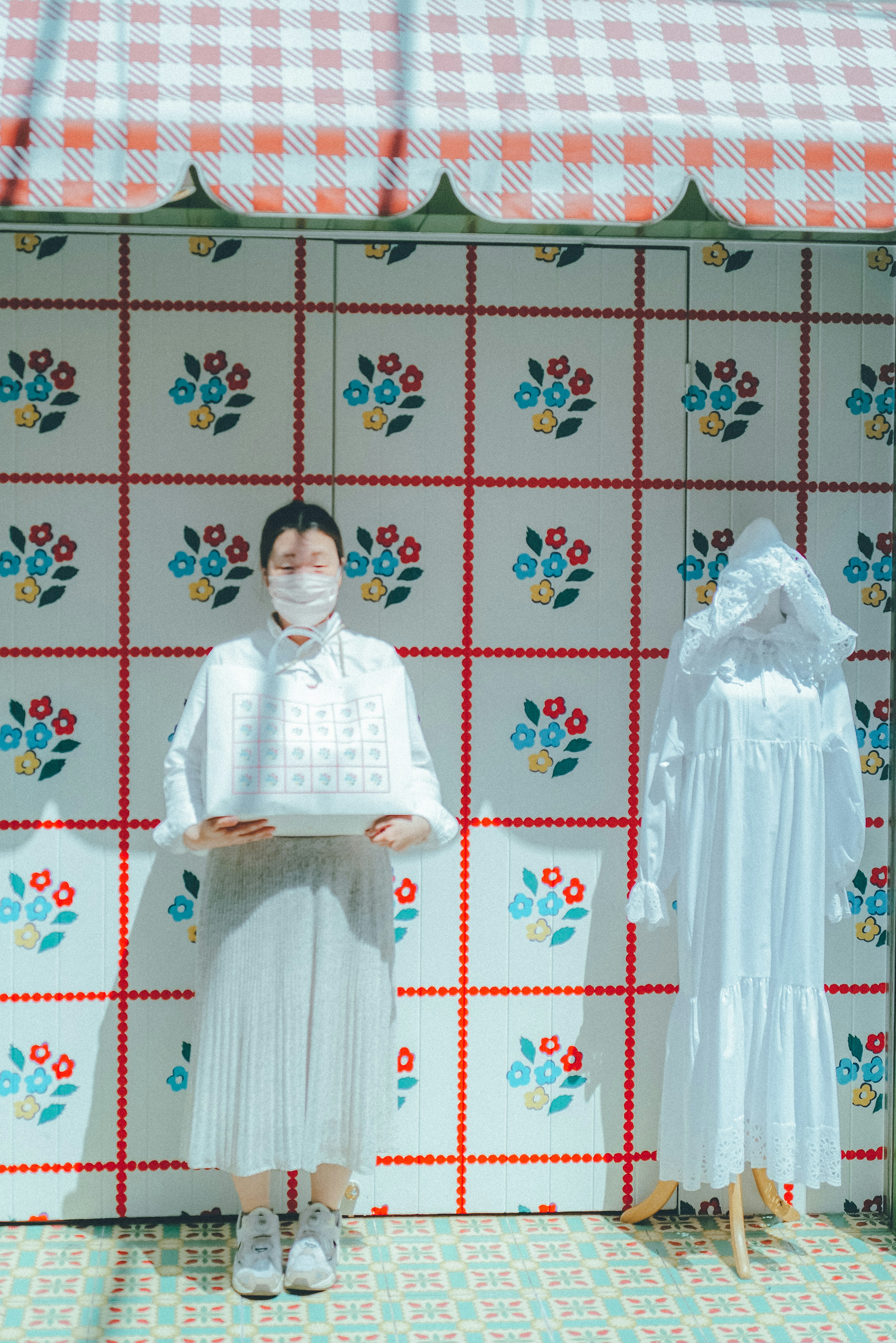 Une femme en vêtements blancs se tenant devant un mur à motifs floraux