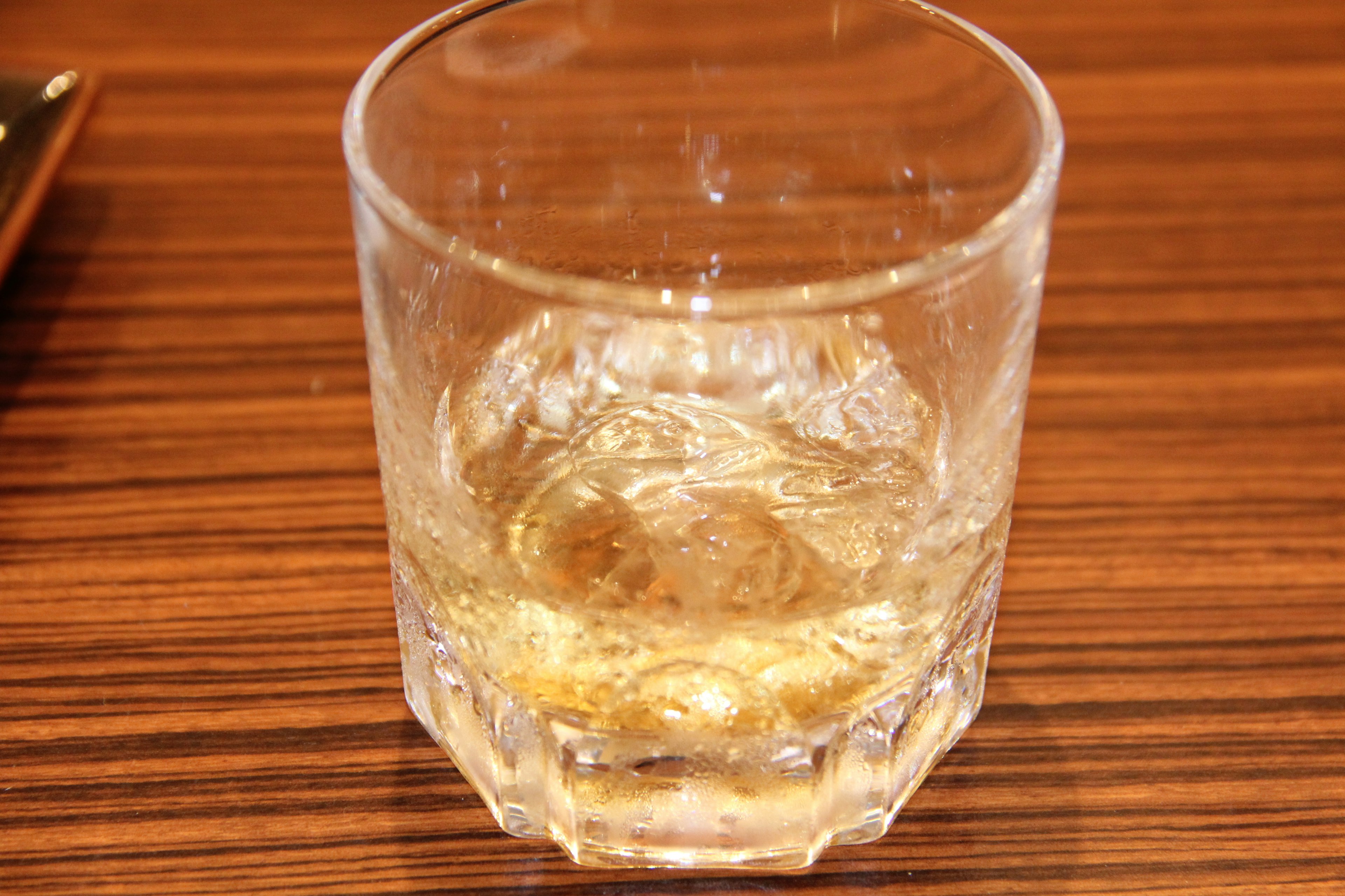 A clear glass containing whiskey and ice on a wooden table